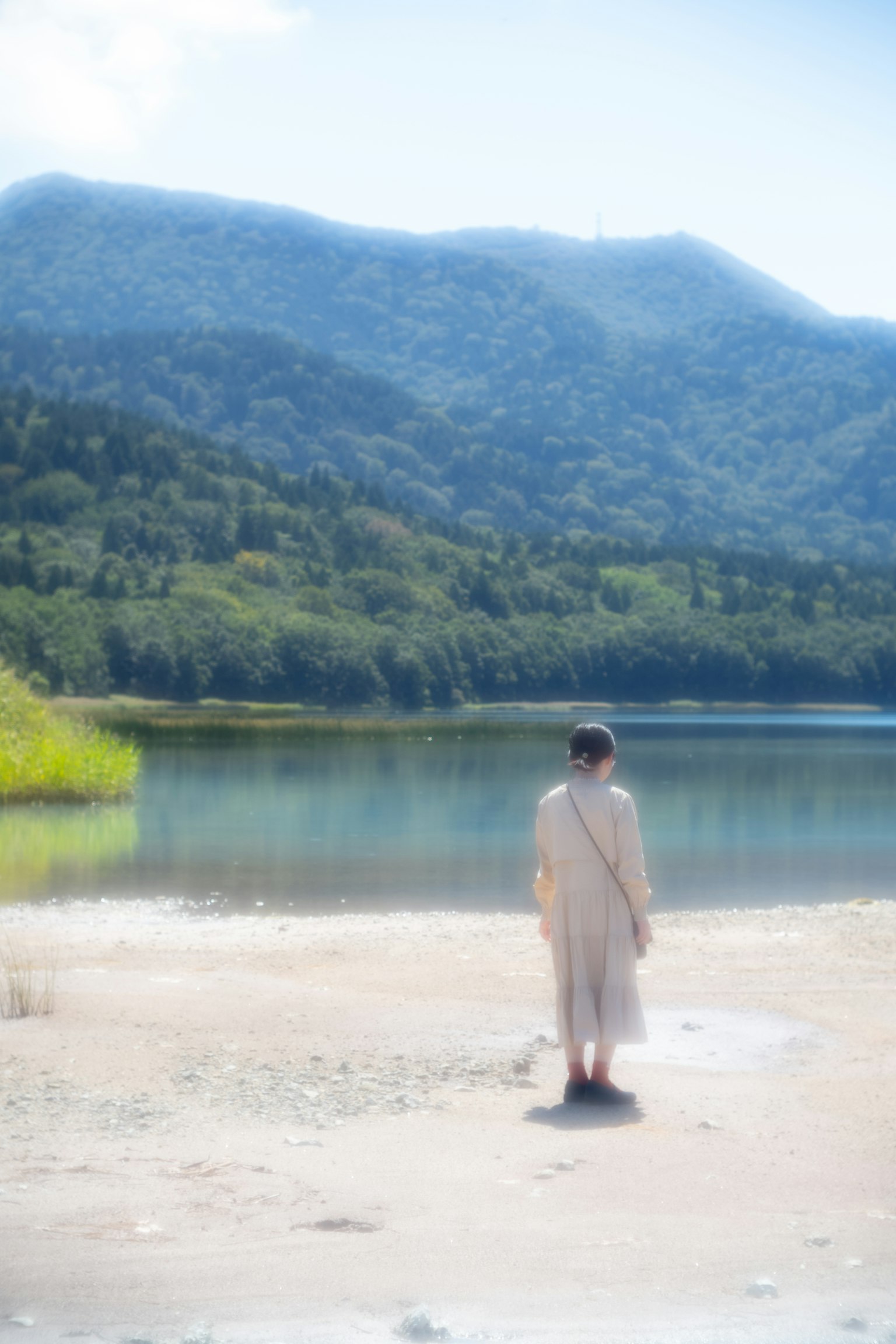 A woman standing by a calm lake lush green mountains in the background