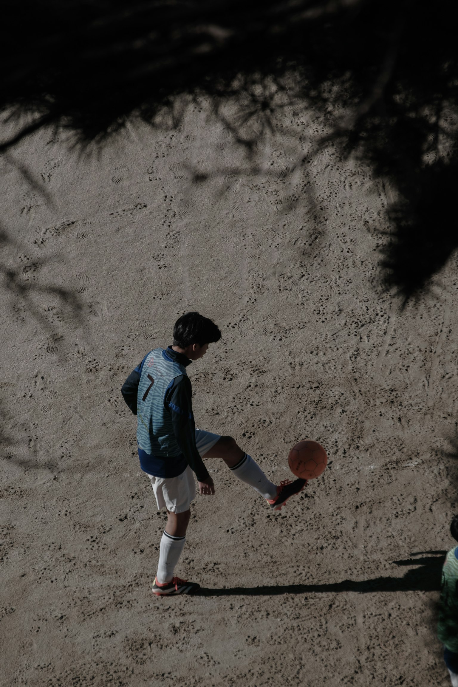 Siluet seorang anak yang menendang bola sepak di lapangan pasir