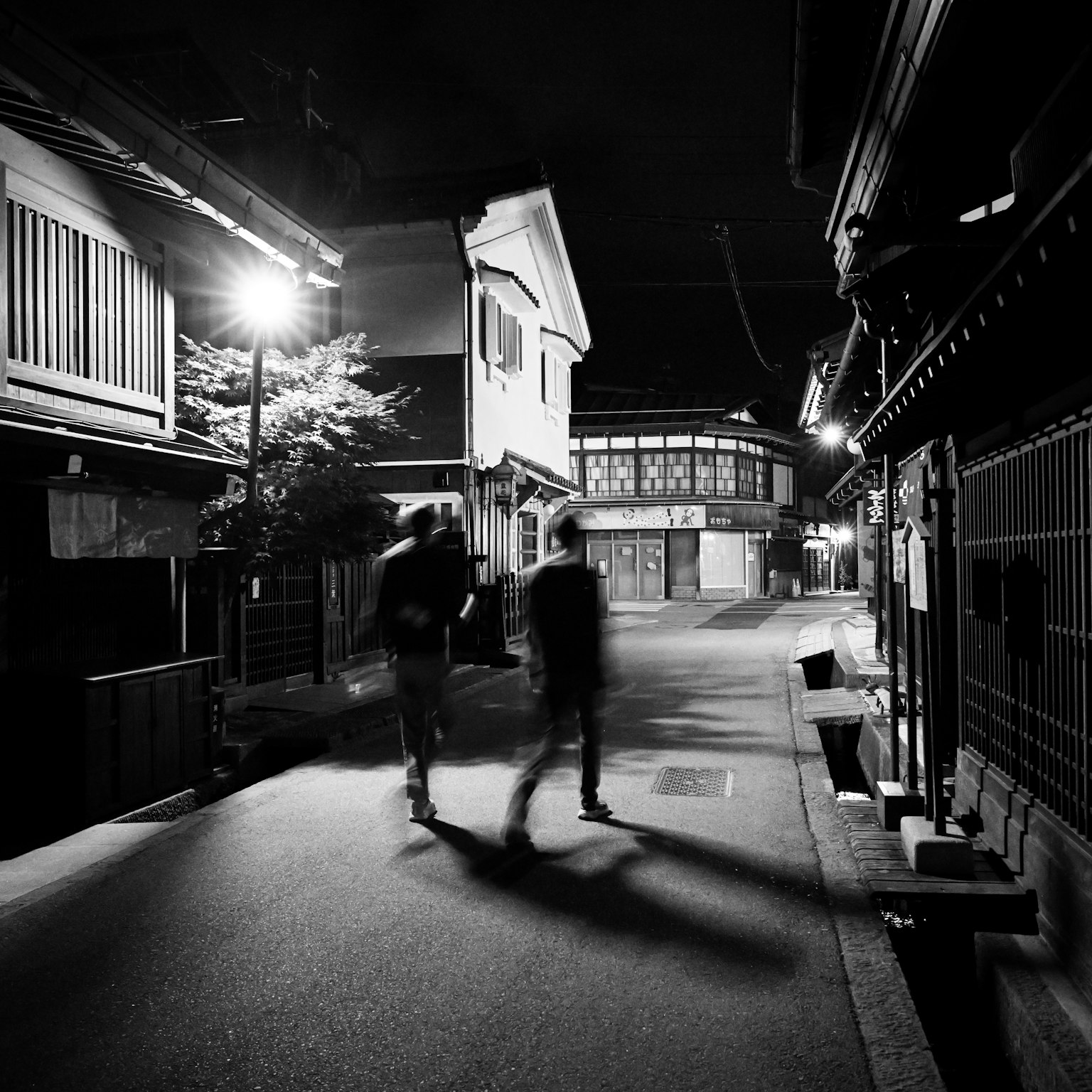 Two silhouettes walking on a quiet street at night with traditional Japanese buildings