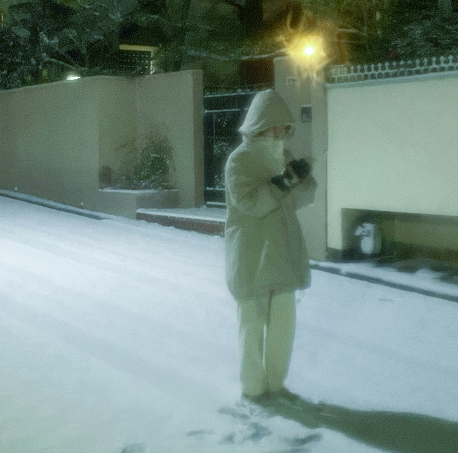 Một người trong áo khoác trắng đứng trong tuyết trên một con phố yên tĩnh