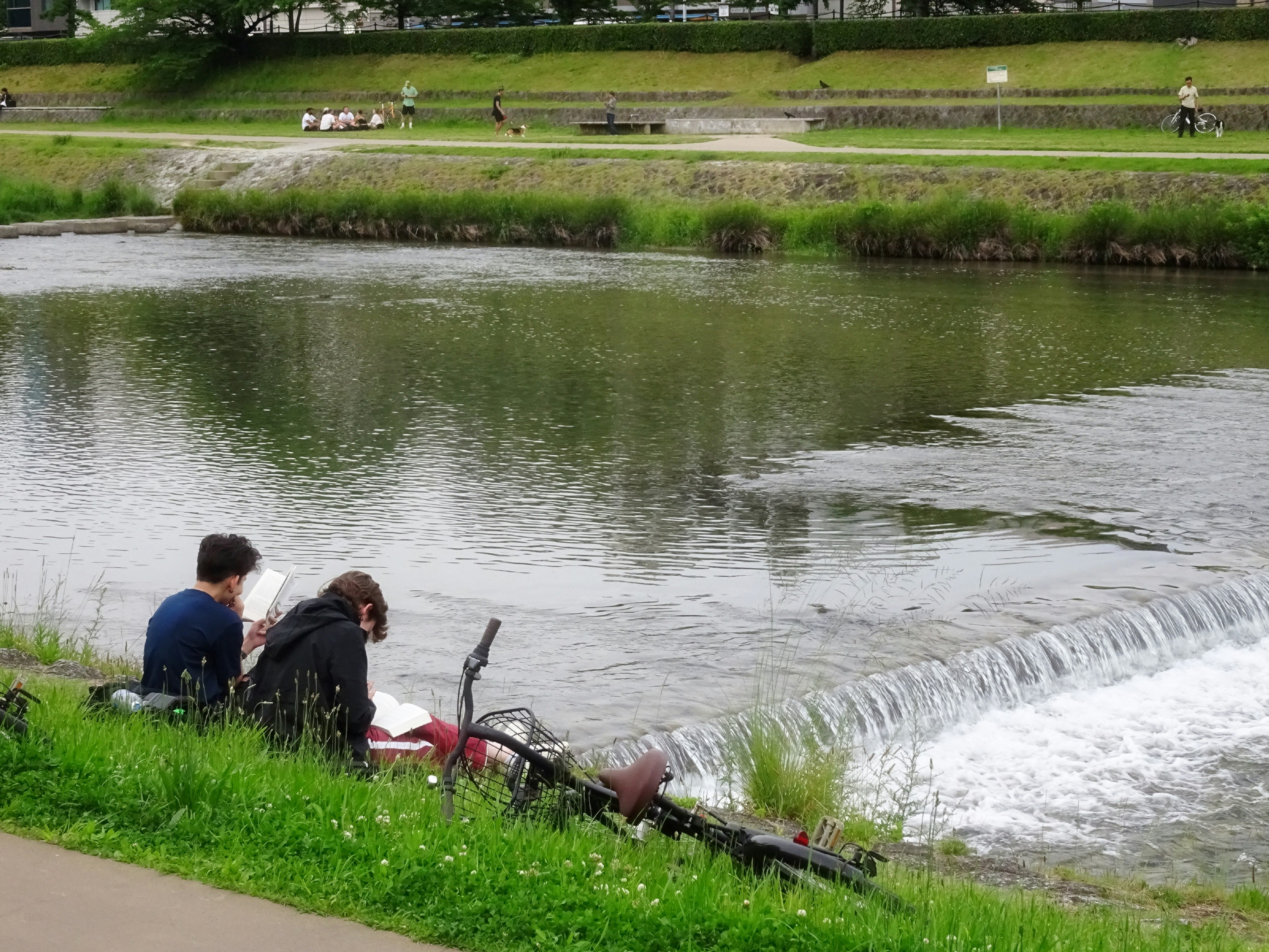 Menschen beim Angeln auf dem Gras am Fluss mit kleinem Wasserfall