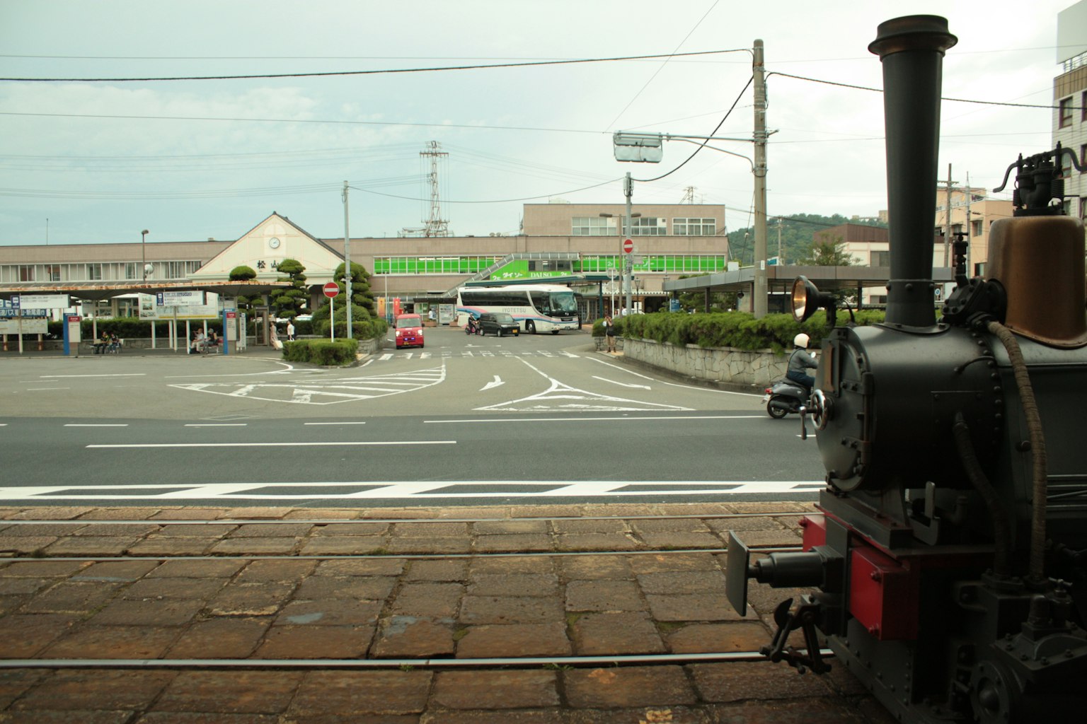 Locomotora de vapor frente a una estación de tren con paisaje circundante