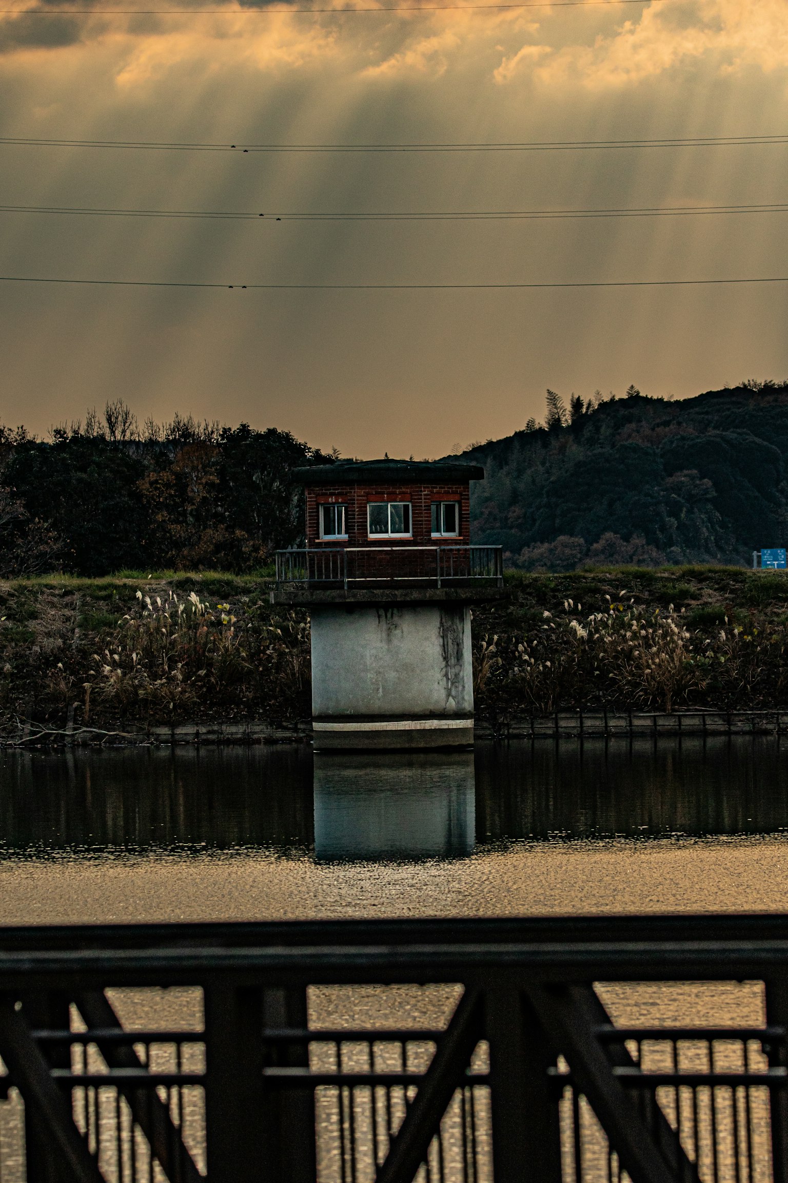 Red-roofed house on a river at dusk with mountains in the background