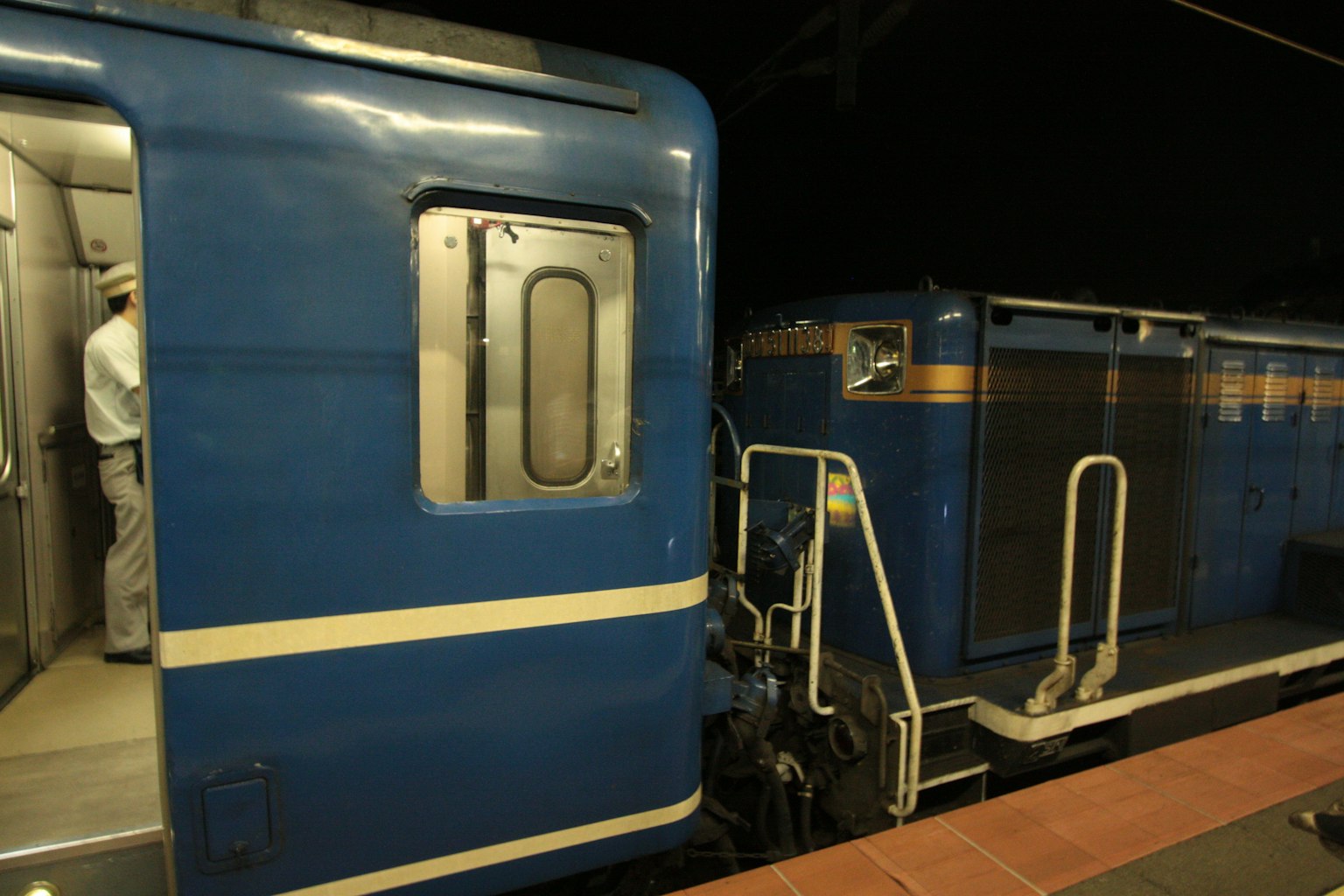 Blue train at a station with visible conductor