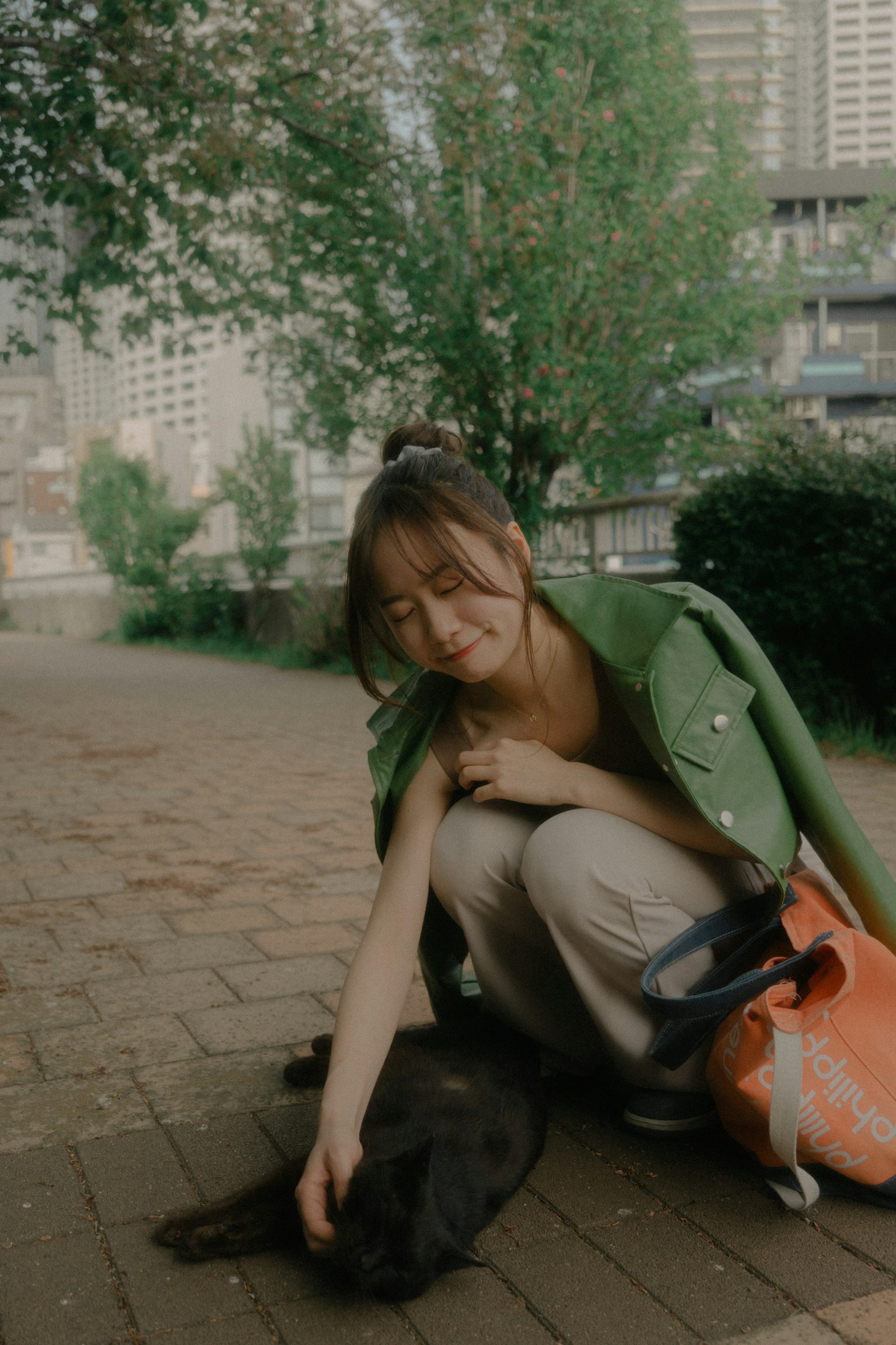 穿綠色外套的女性在公園裡撫摸一隻黑狗