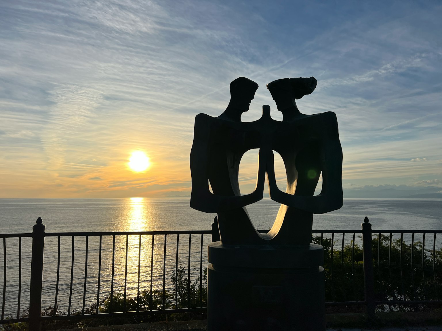 Scultura astratta di due figure che si fronteggiano con il tramonto sull'oceano
