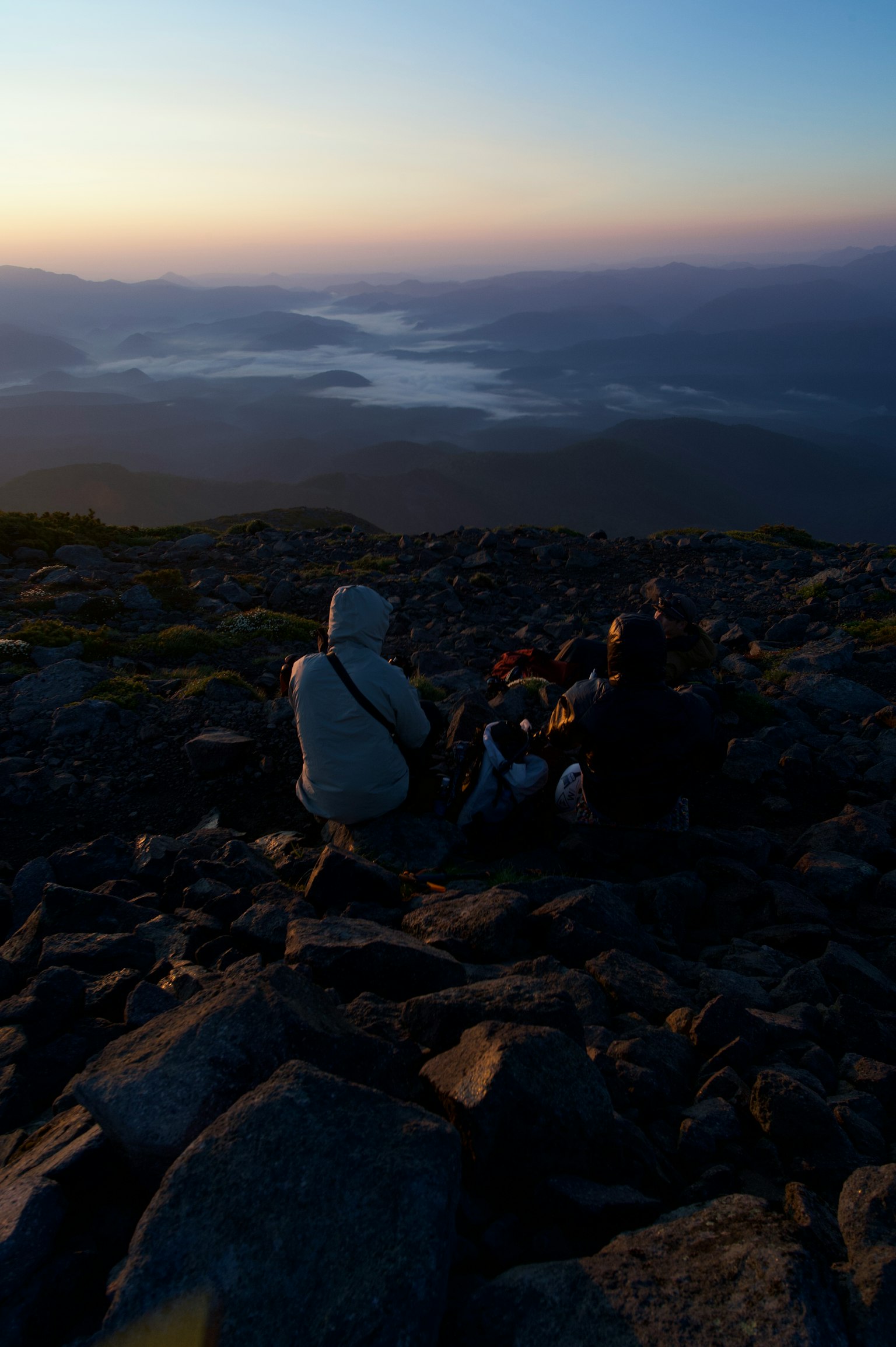 Two people enjoying the view from a mountain peak with a lake in the background