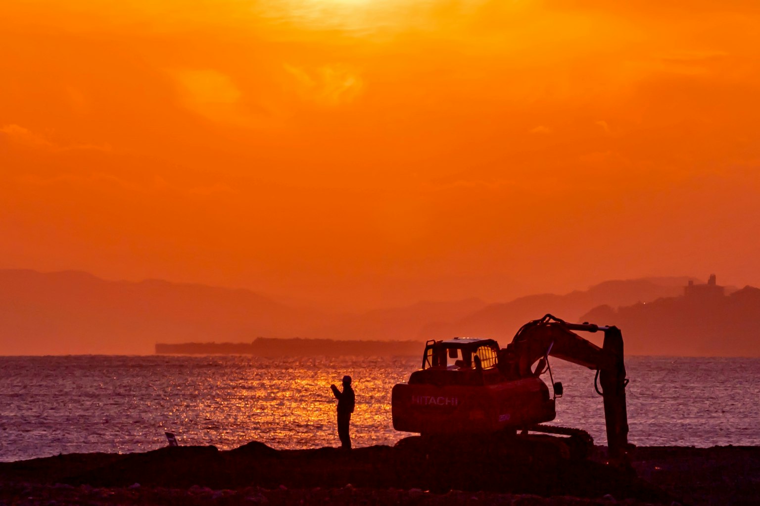 Sonnenuntergangsansicht eines Strandes mit schwerem Gerät und einem Arbeiter
