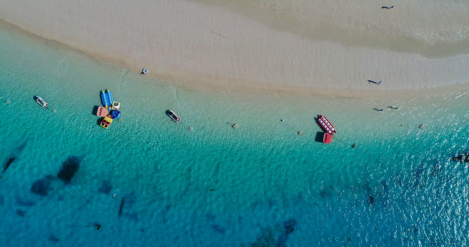 Vista aérea de una playa con agua turquesa y arena blanca botes coloridos alineados