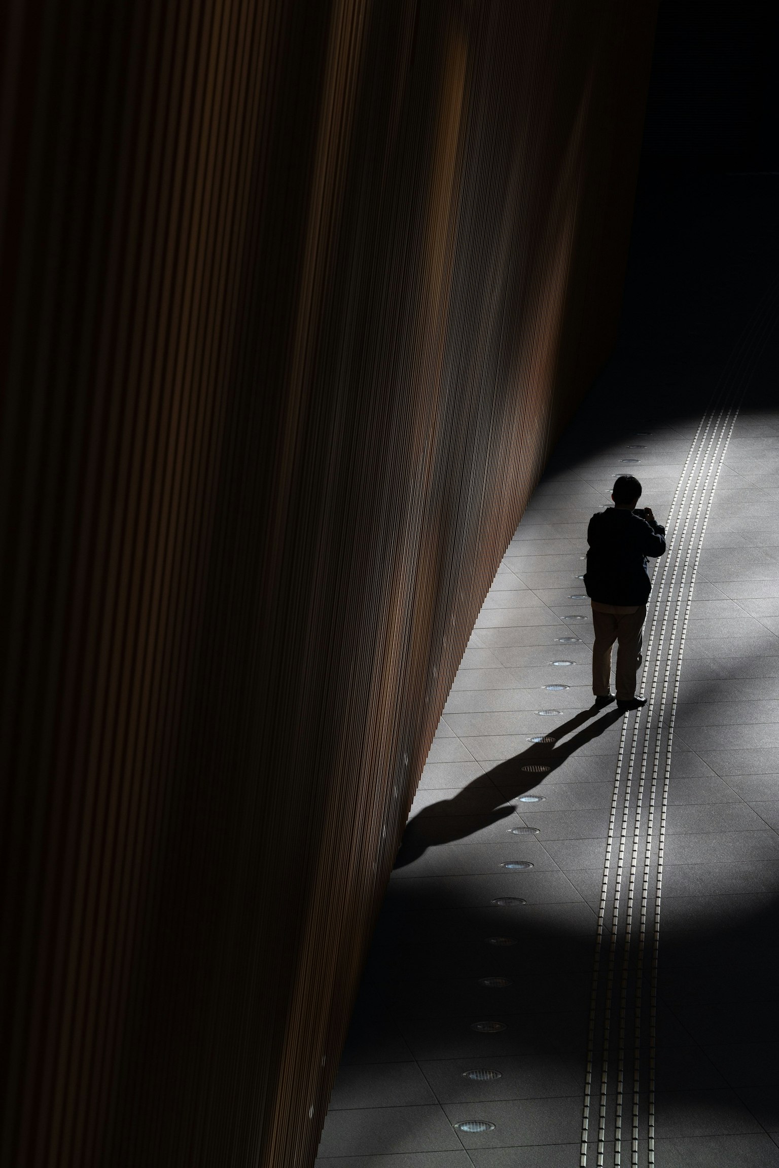 Una persona de pie en la sombra con un fuerte contraste de luz en un entorno urbano