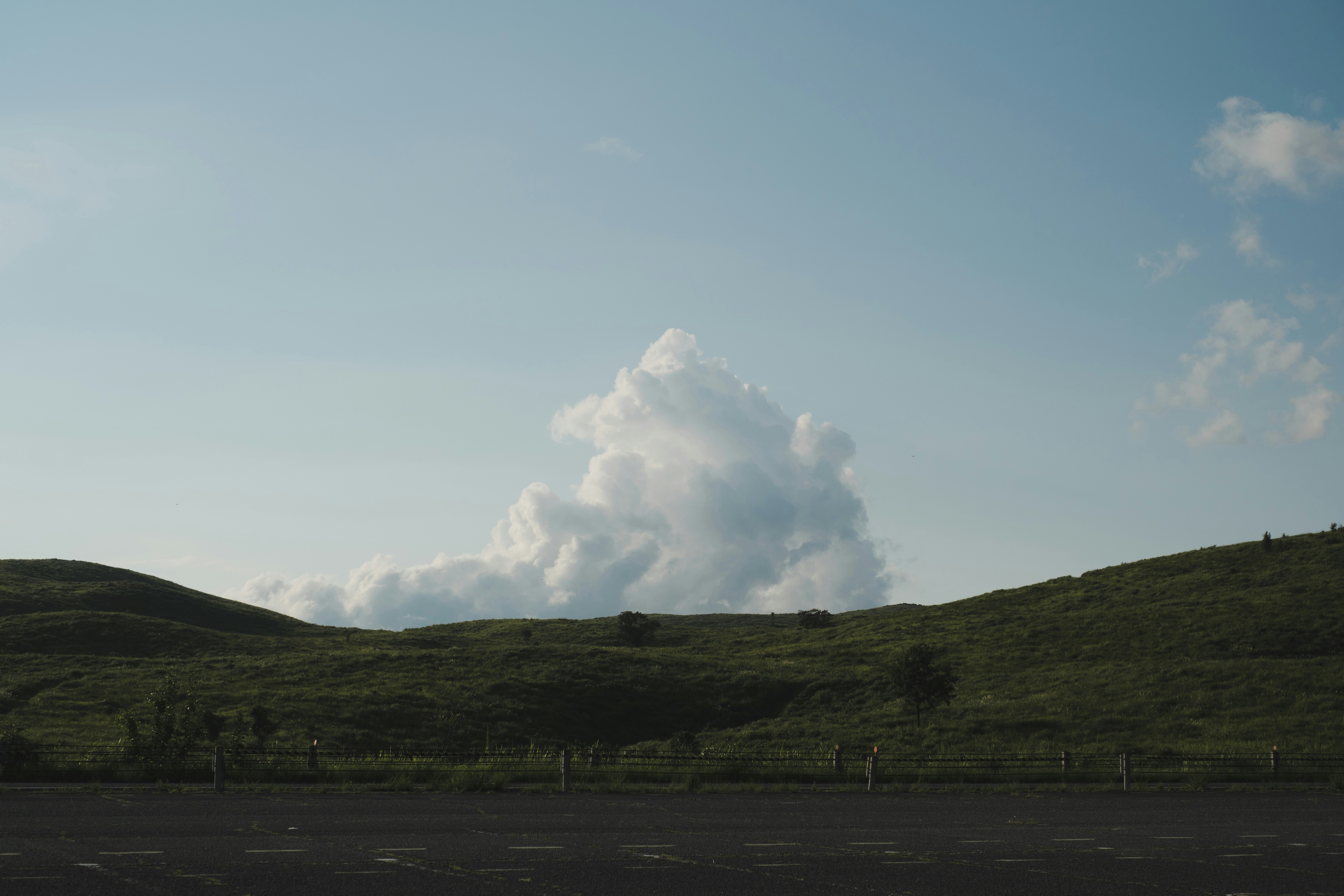 丘陵の牧草地に立つ煙の上がる火山のような噴煙