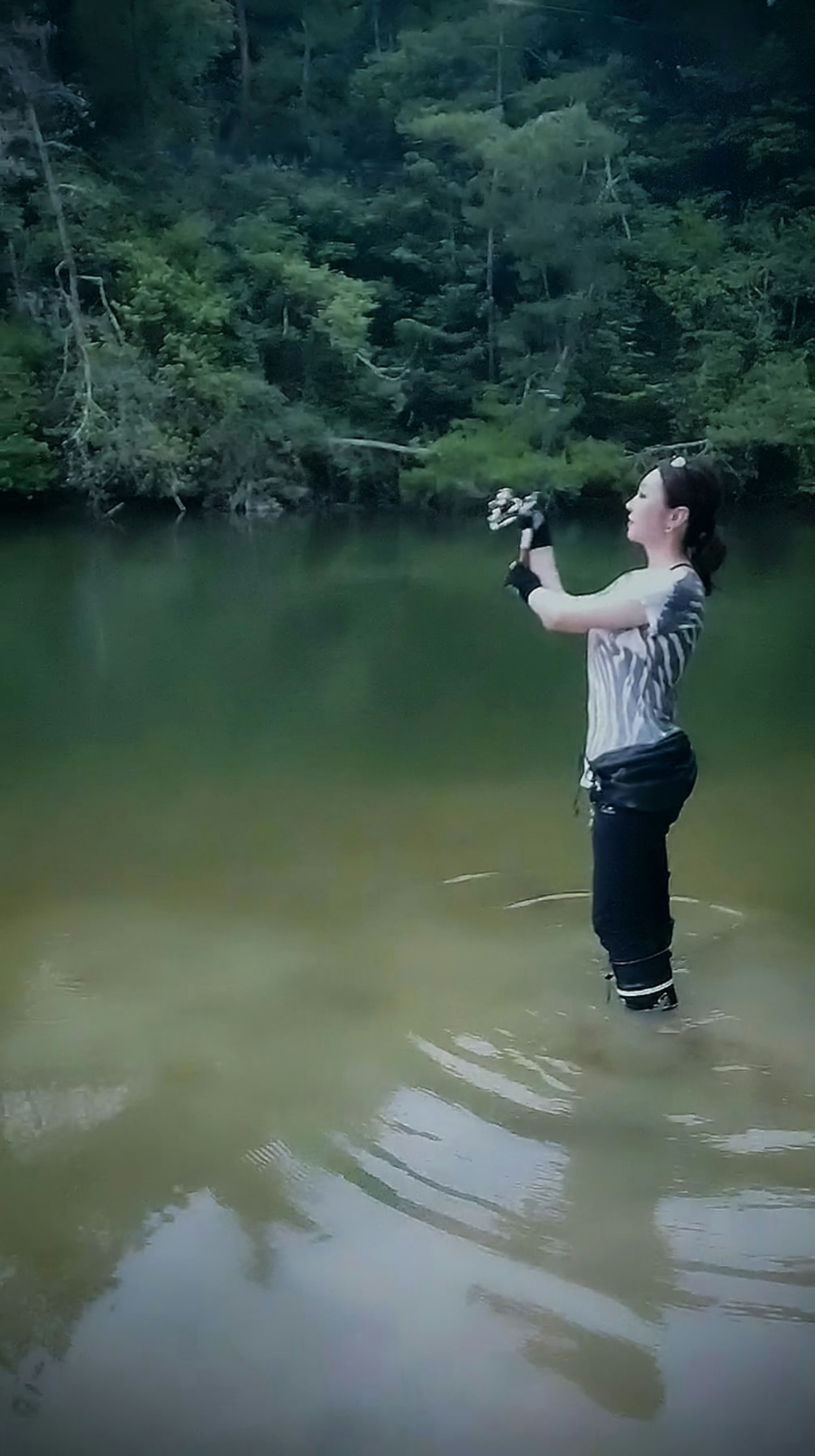 Una mujer pescando en agua poco profunda rodeada de árboles
