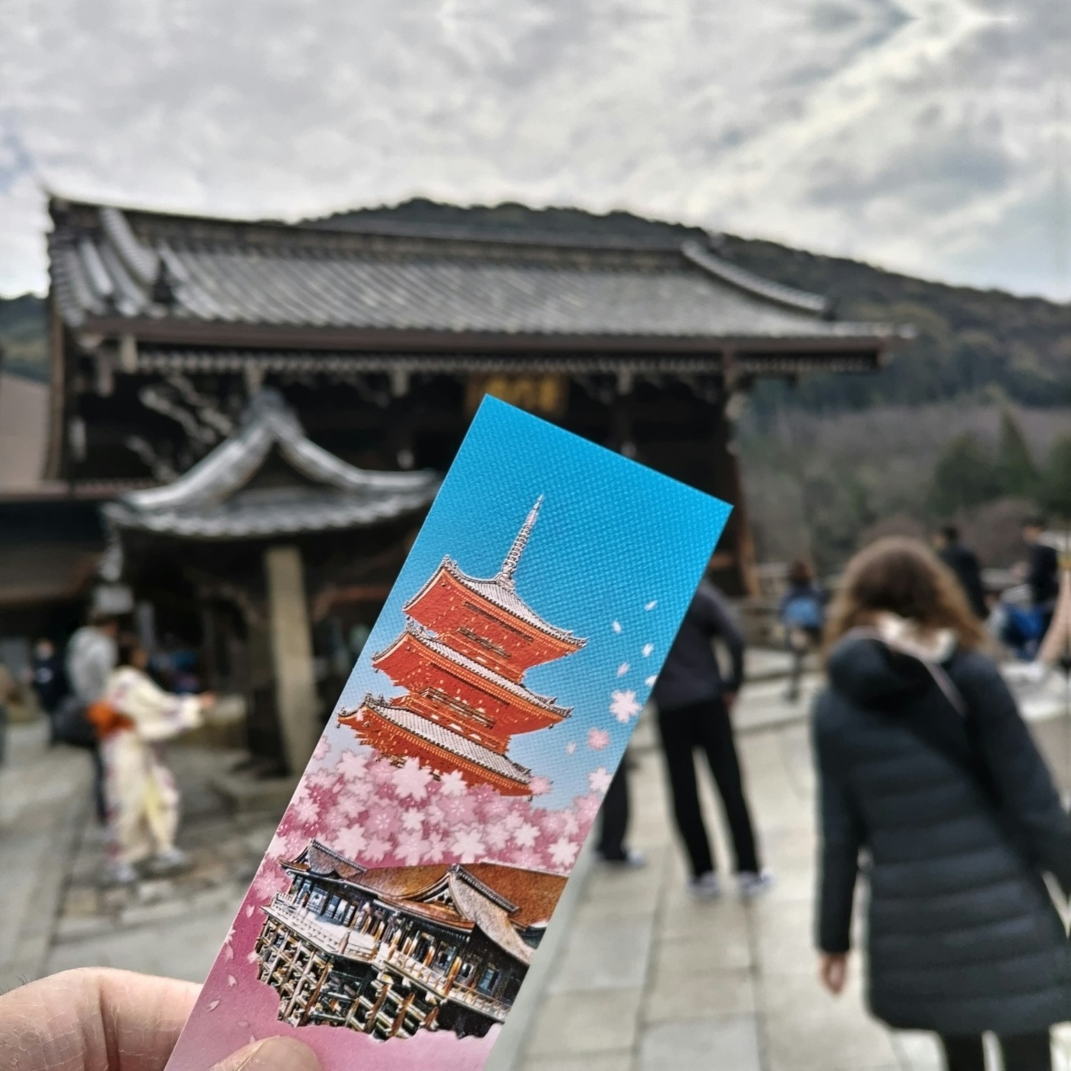 A person holding a bookmark featuring cherry blossoms with an ancient temple in the background
