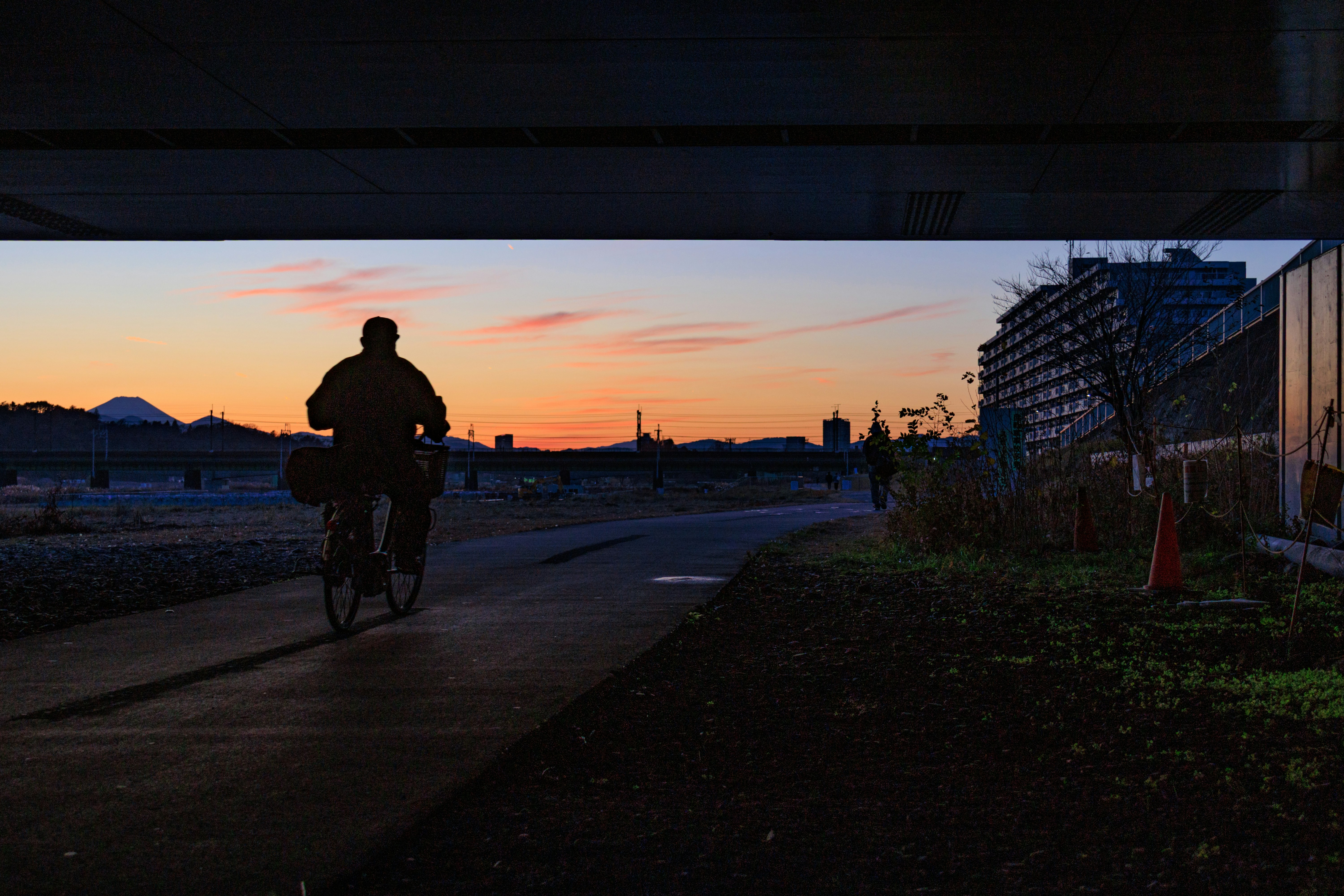 是政橋の夕暮れに自転車で走る人のシルエットのある川沿いの道