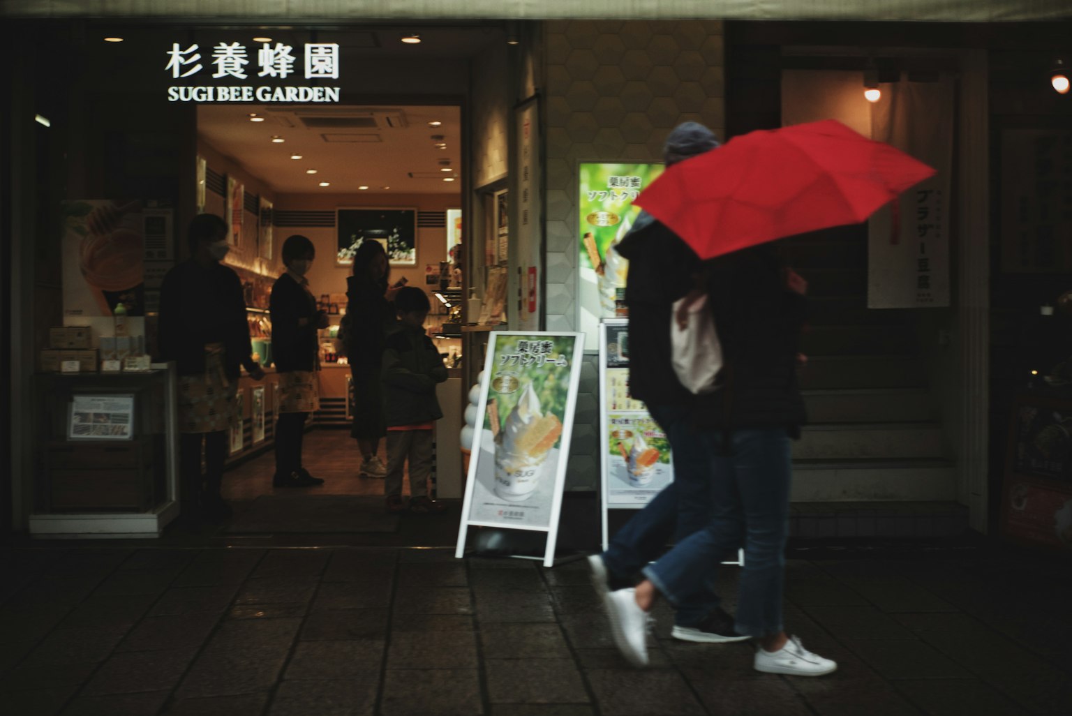 Person holding a red umbrella walking in front of a sushi restaurant