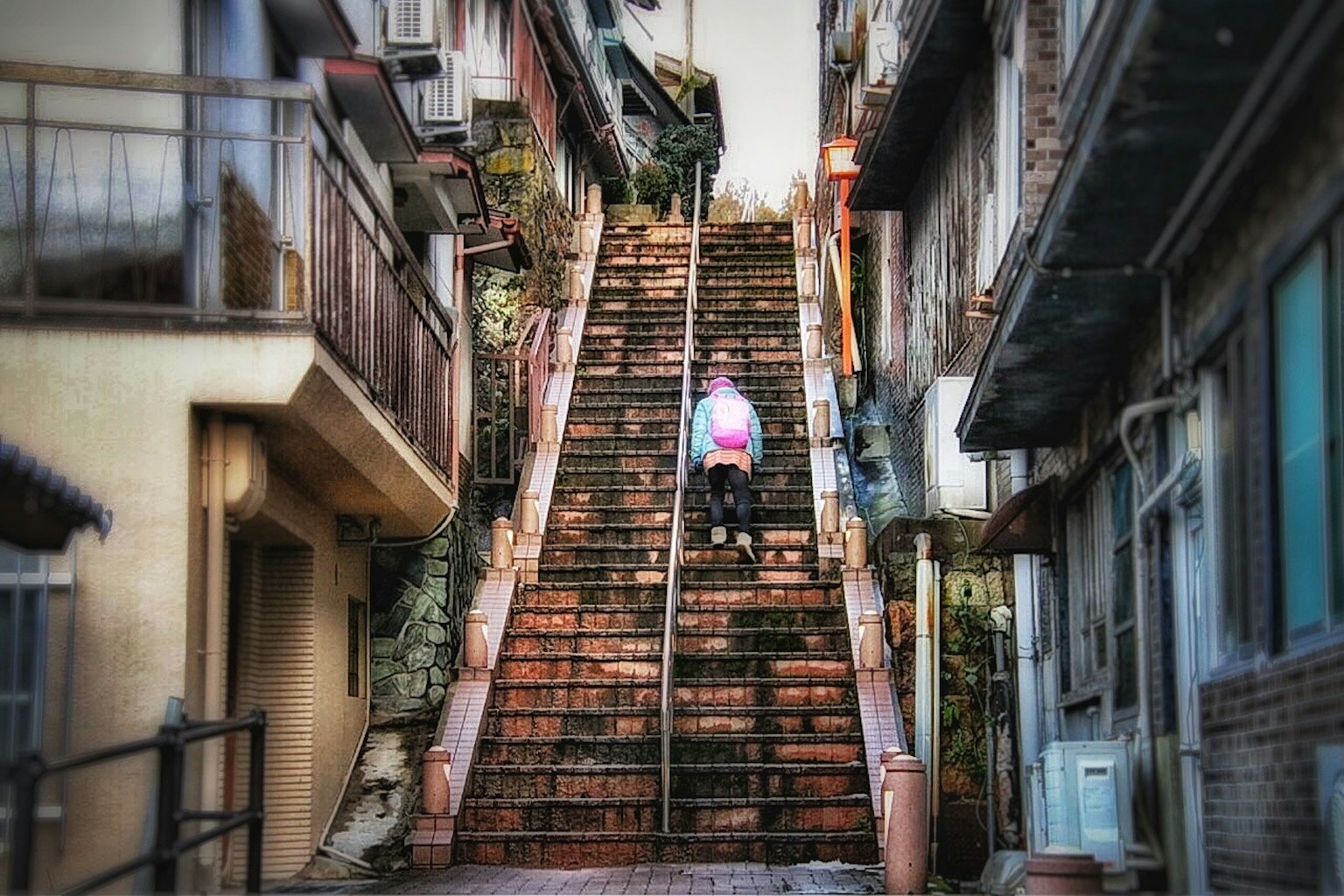 A person walking up an old staircase surrounded by buildings