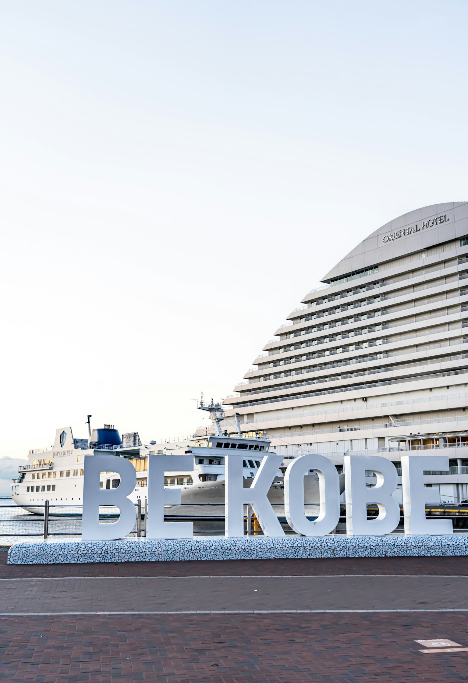Bảng chữ lớn 'BE KOBE' tại cảng Kobe với một con tàu ở phía sau
