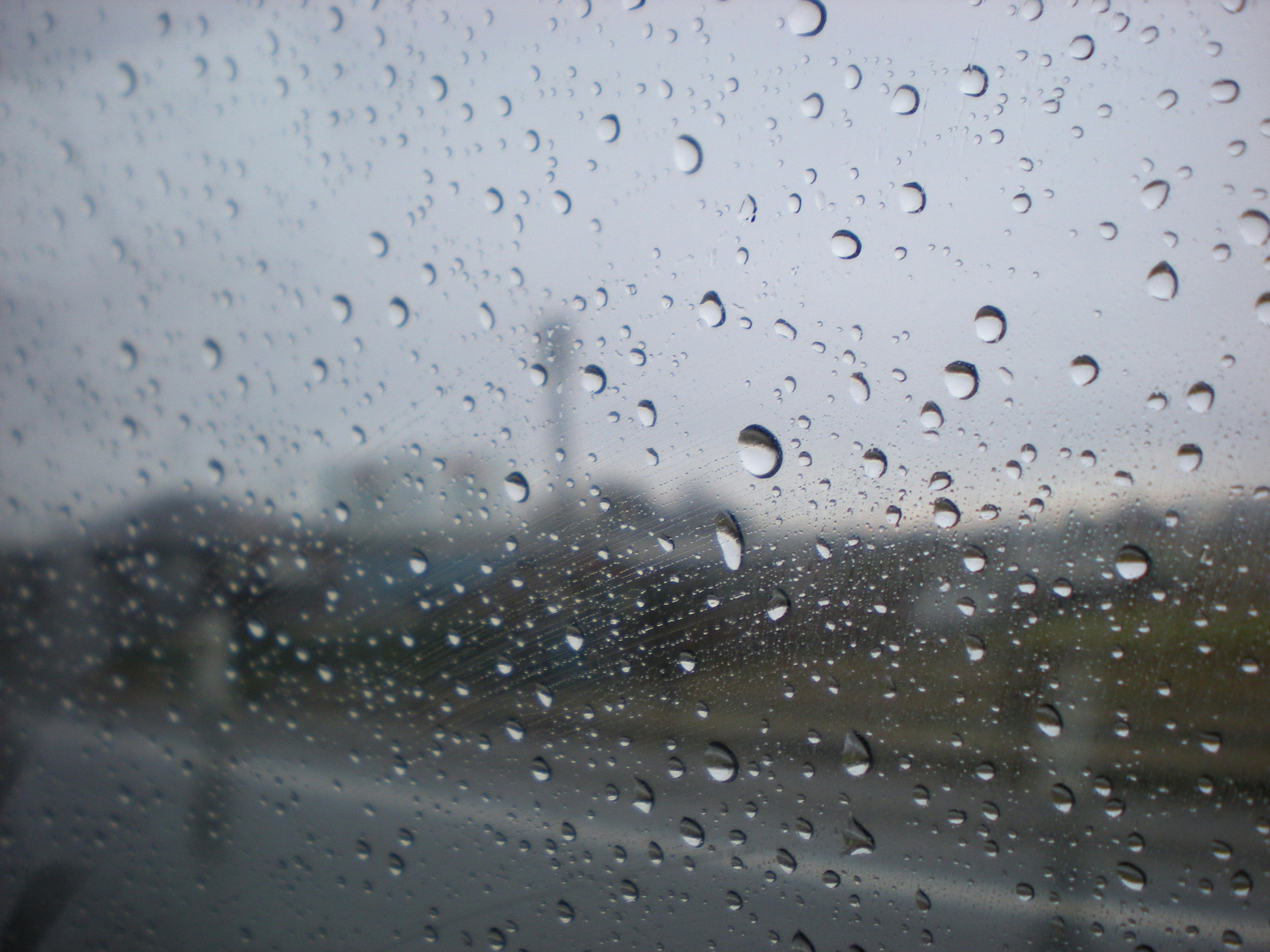 Regentropfen auf einem Fenster mit bewölktem Himmel dahinter