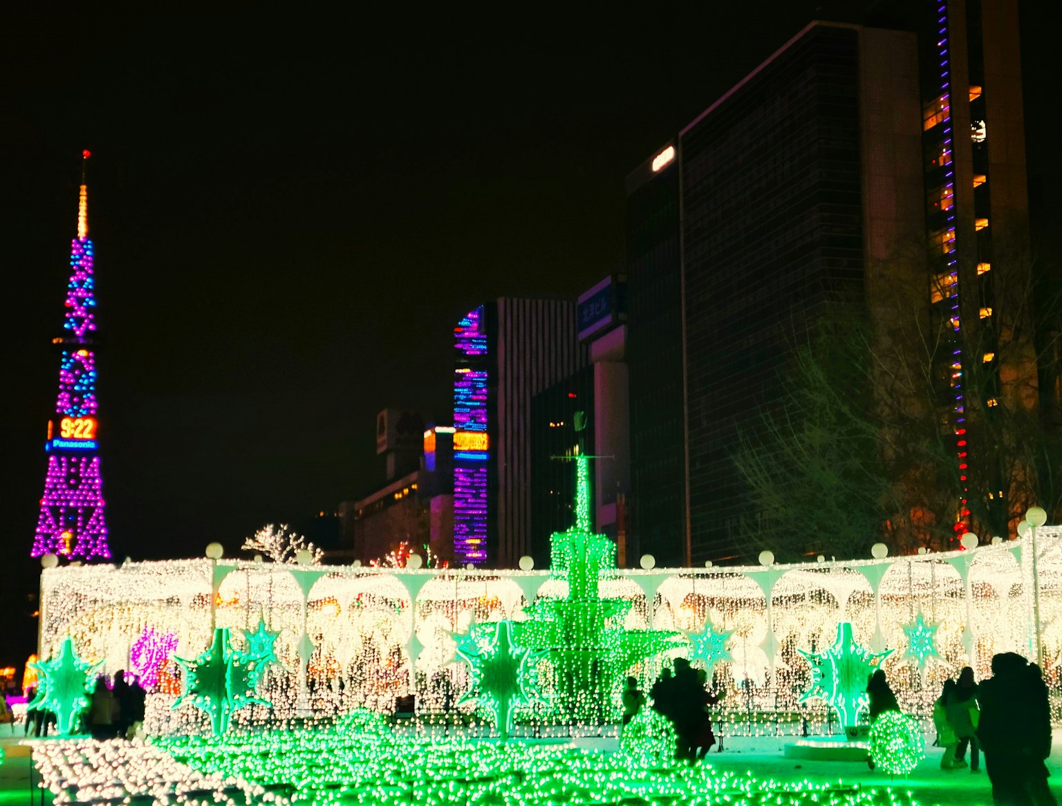 ภาพยามค่ำคืนที่มีชีวิตชีวาพร้อมไฟวันหยุดหลากสีและต้นคริสต์มาสขนาดใหญ่