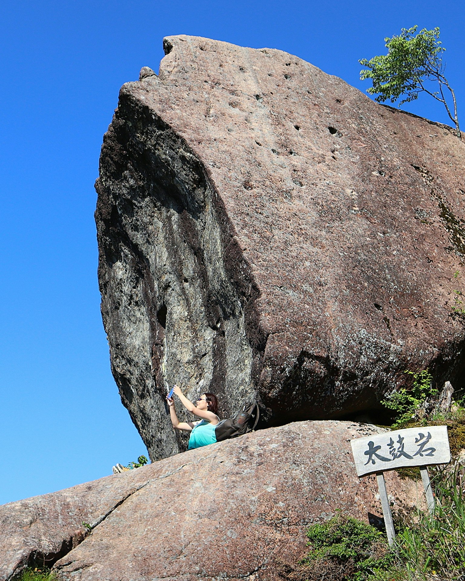 Person bouldering in front of a large rock under a blue sky natural scenery