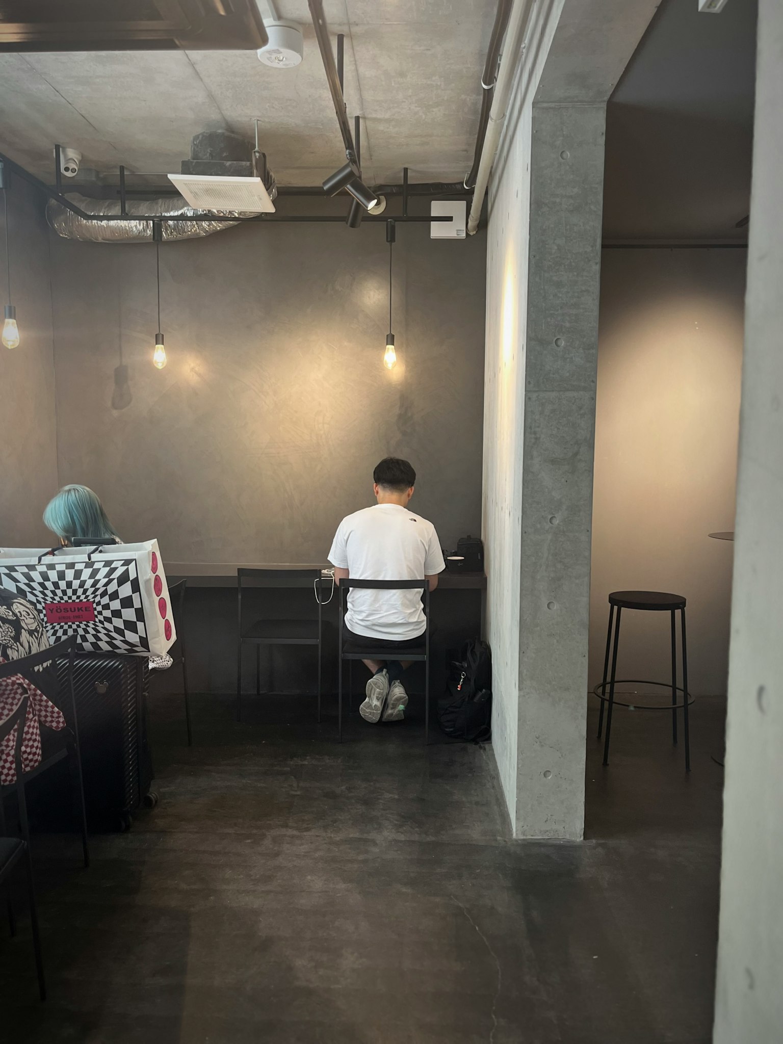 ชายคนหนึ่งทำงานที่ร้านกาแฟโดยมีผู้หญิงนั่งอยู่ใกล้ ๆ แสงไฟอุ่นสร้างบรรยากาศที่อบอุ่น