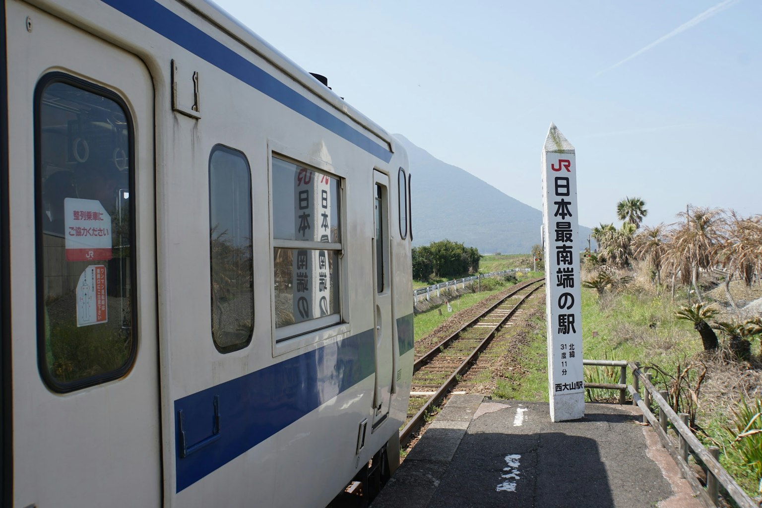 Sisi kereta yang berhenti di stasiun pedesaan Jepang dengan tanda