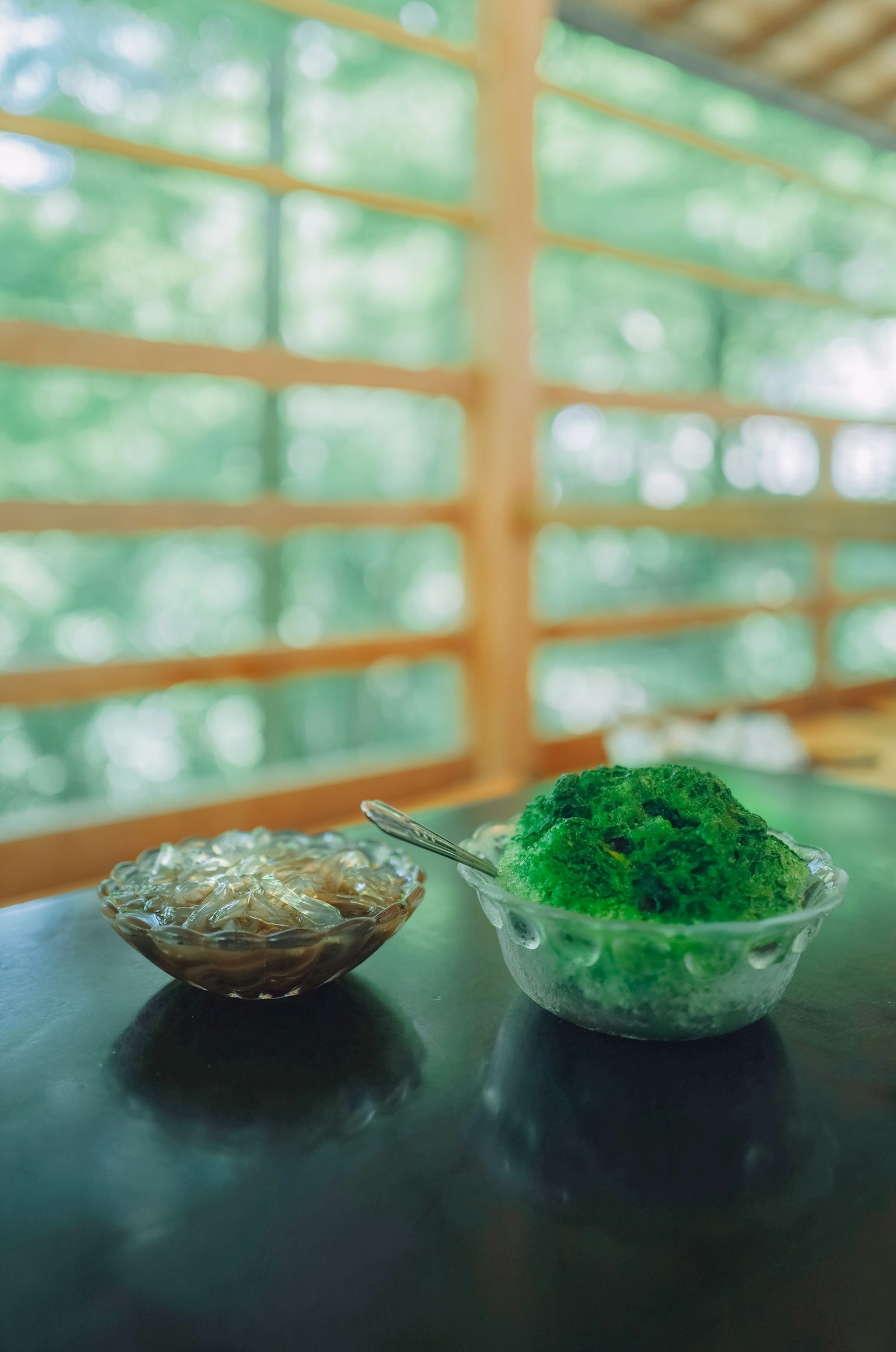 อาหารสีเขียวในชามใสและอาหารสีน้ำตาลในจานเล็กบนโต๊ะที่มีหน้าต่างไม้ด้านหลัง