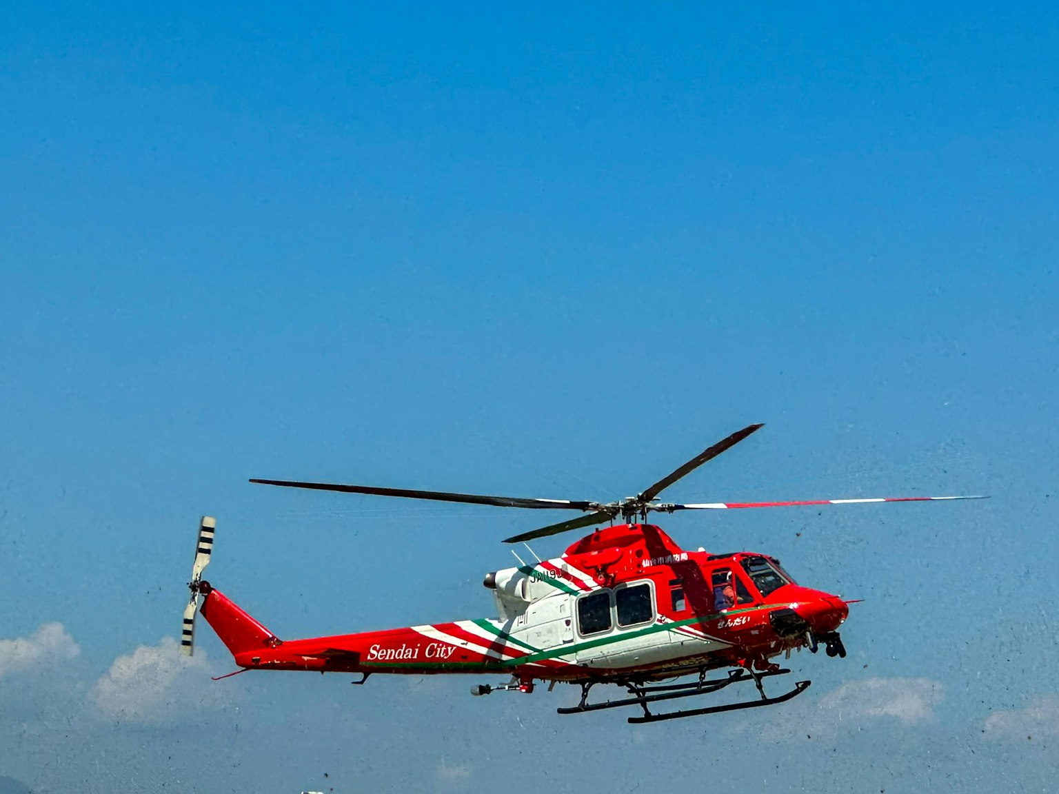 Helikopter merah dan putih terbang melawan langit biru