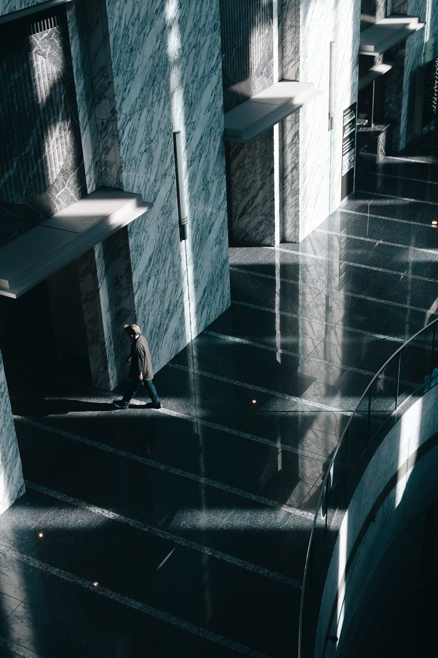 Una persona caminando en el interior de un edificio moderno con suelo de mármol y luces y sombras entrelazadas