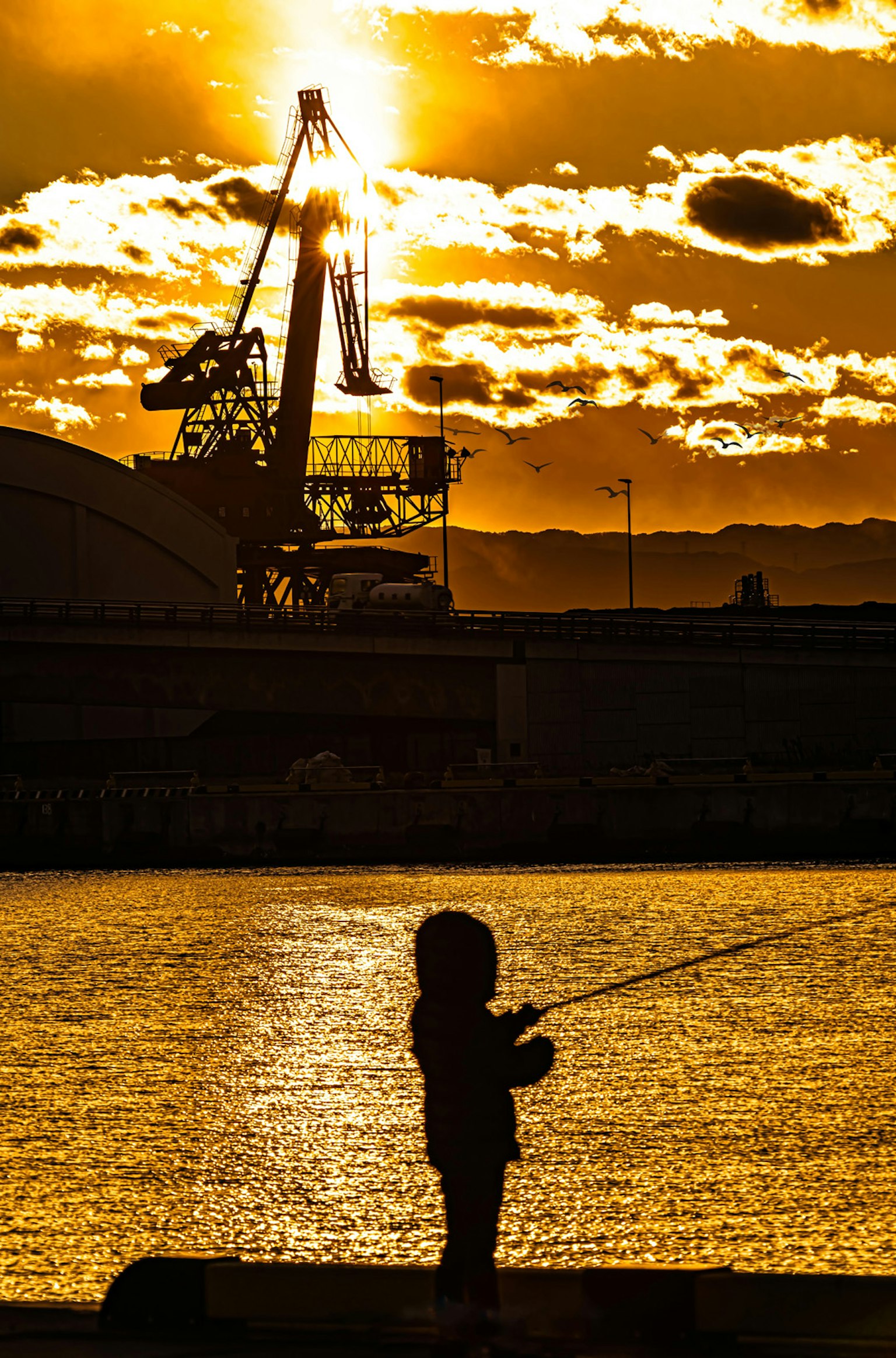 Silhouette eines Kindes, das gegen einen Sonnenuntergang fischt