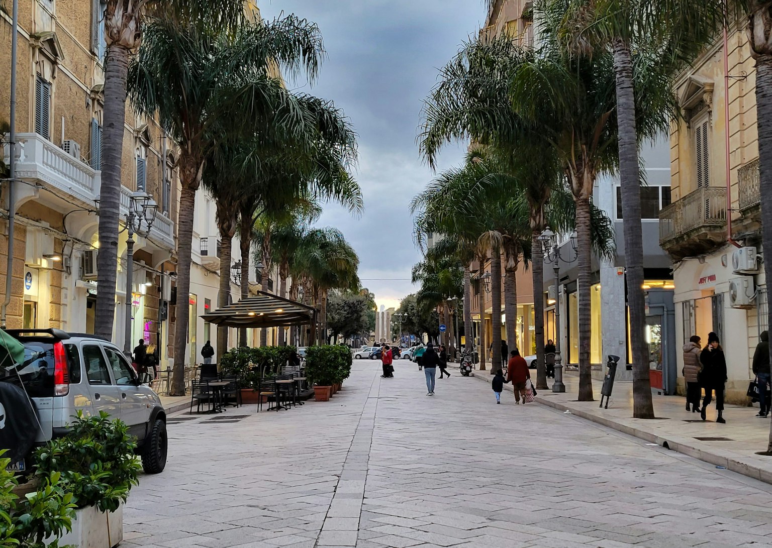Strada fiancheggiata da palme Persone che camminano sotto un cielo nuvoloso