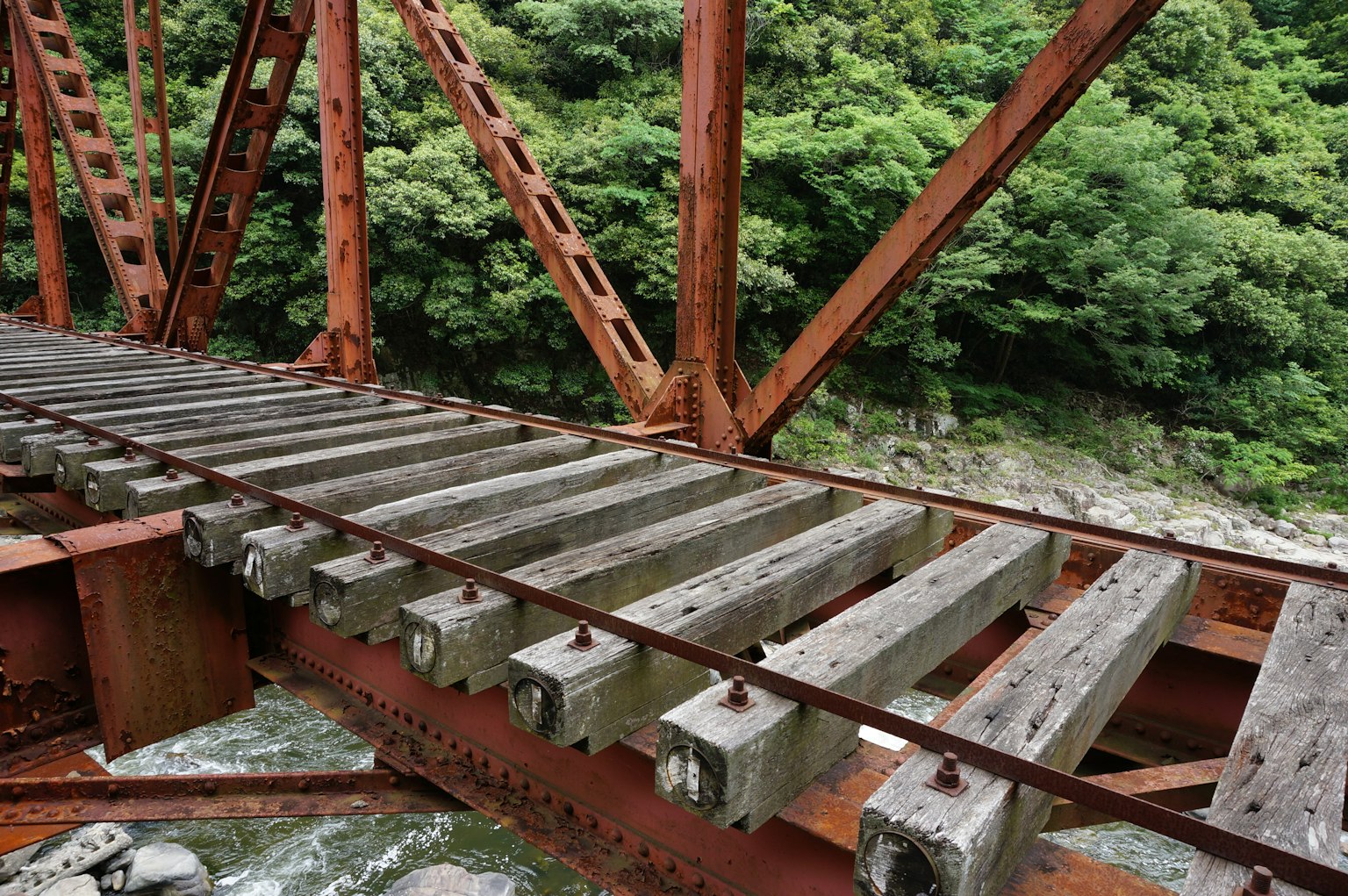Jembatan besi berkarat dengan papan kayu dan latar belakang hijau subur