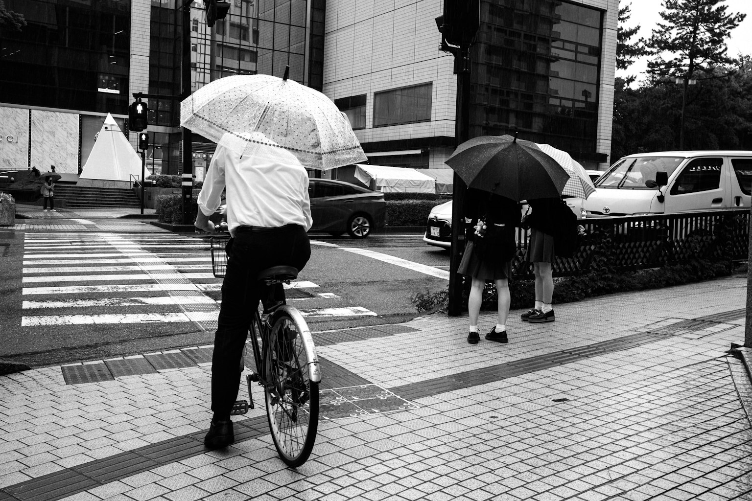 Foto en blanco y negro de un hombre en bicicleta con un paraguas y peatones sosteniendo paraguas bajo la lluvia