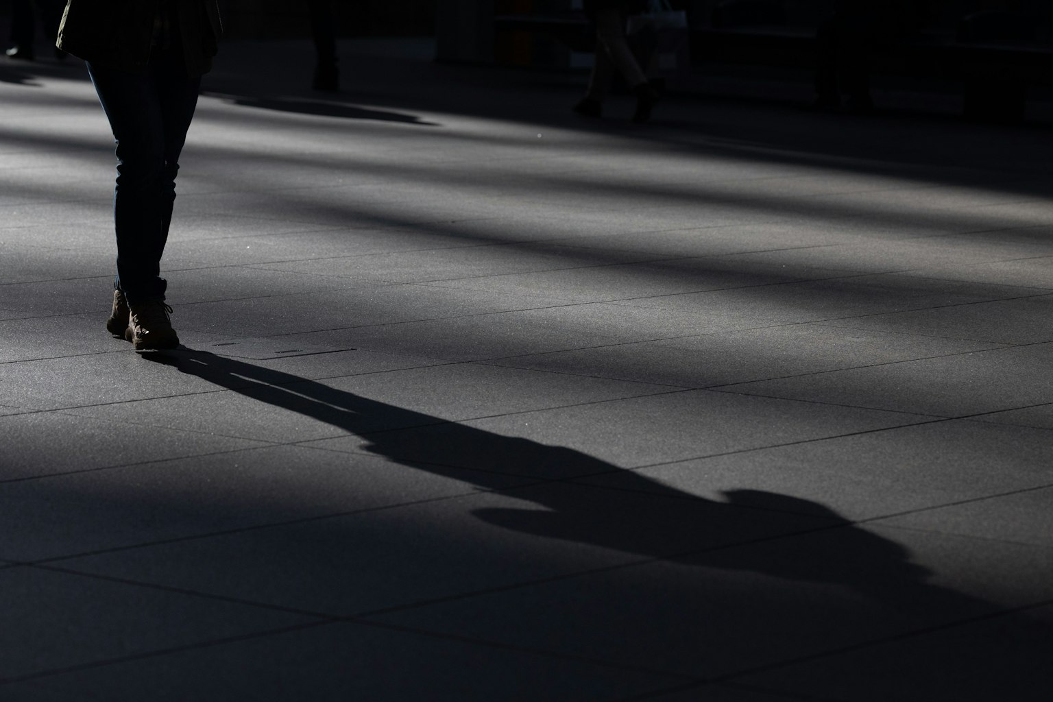 Silueta de un peatón proyectando una sombra sobre una acera iluminada por el sol