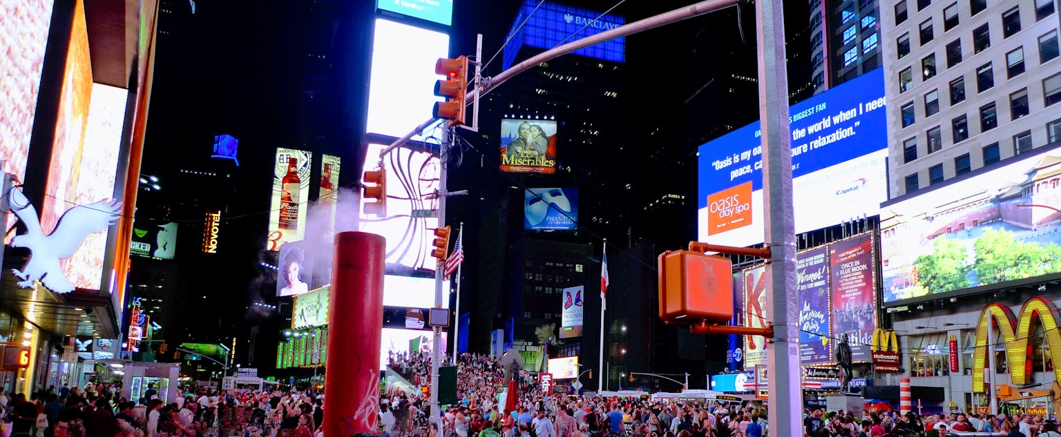 Pemandangan malam yang ramai di Times Square dengan papan iklan besar dan kerumunan orang