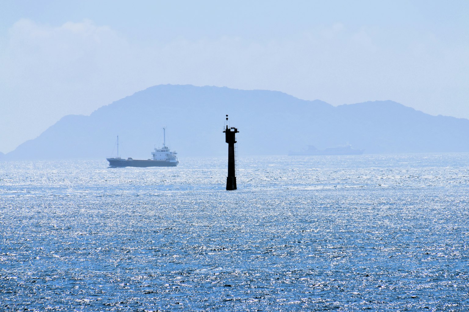 Faro en el agua con un barco y una isla lejana