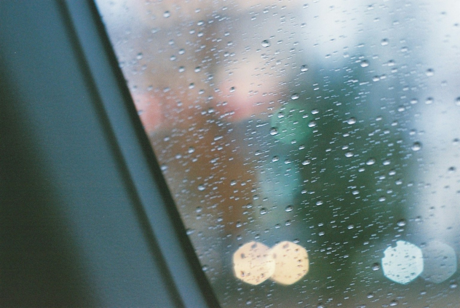ภาพของหยดน้ำฝนบนหน้าต่างพร้อมแสงไฟเมืองที่เบลออยู่ด้านหลัง