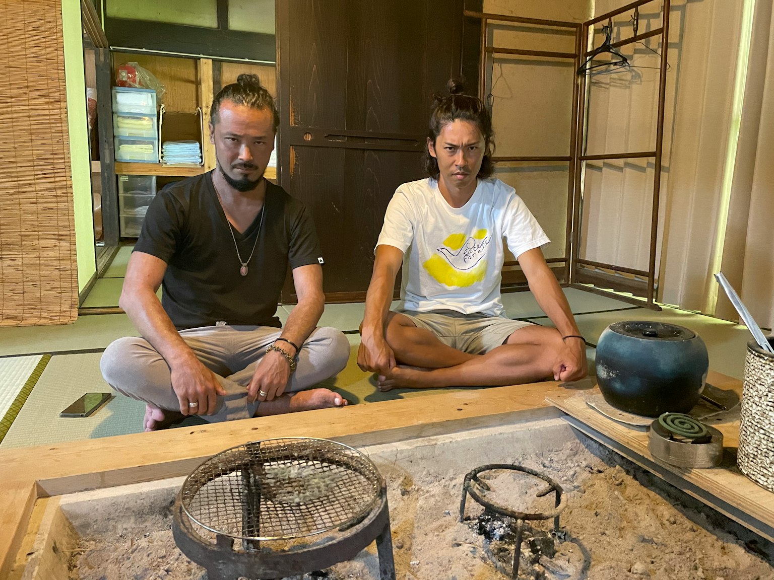 两名男性坐在日本风格的房间里，显露出一个凹陷的火炉