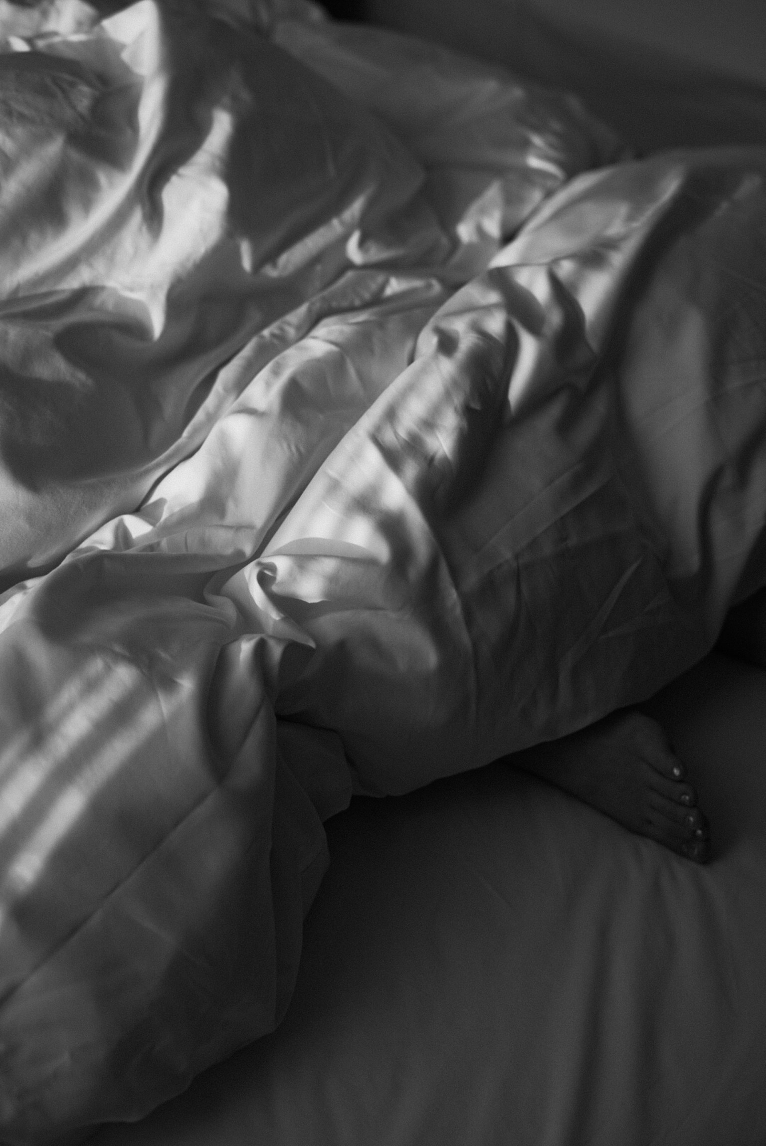 Monochrome photo of sheets and blanket with beautiful shadows on a bed