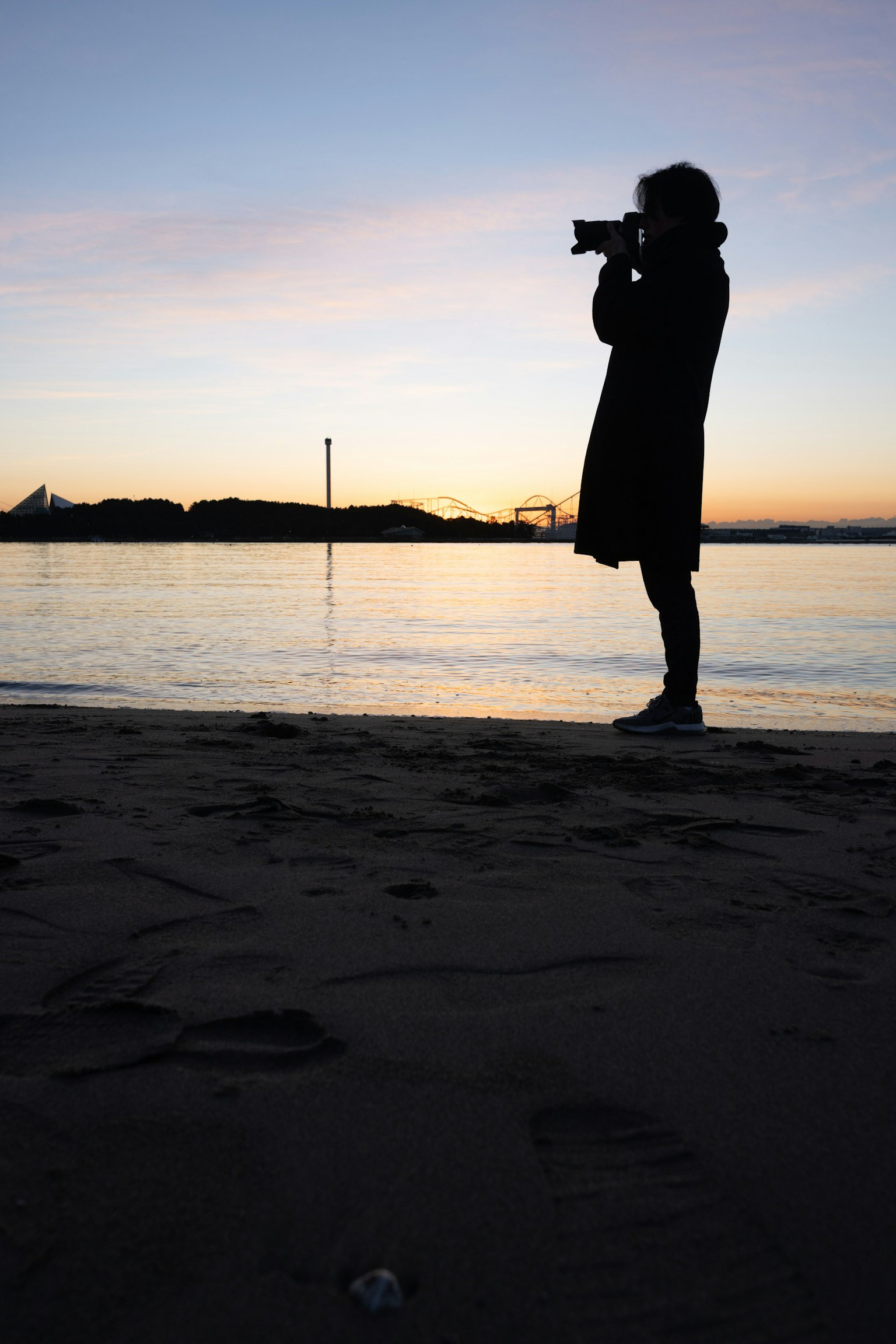 Silhouette of a person holding a camera standing on the beach at sunset