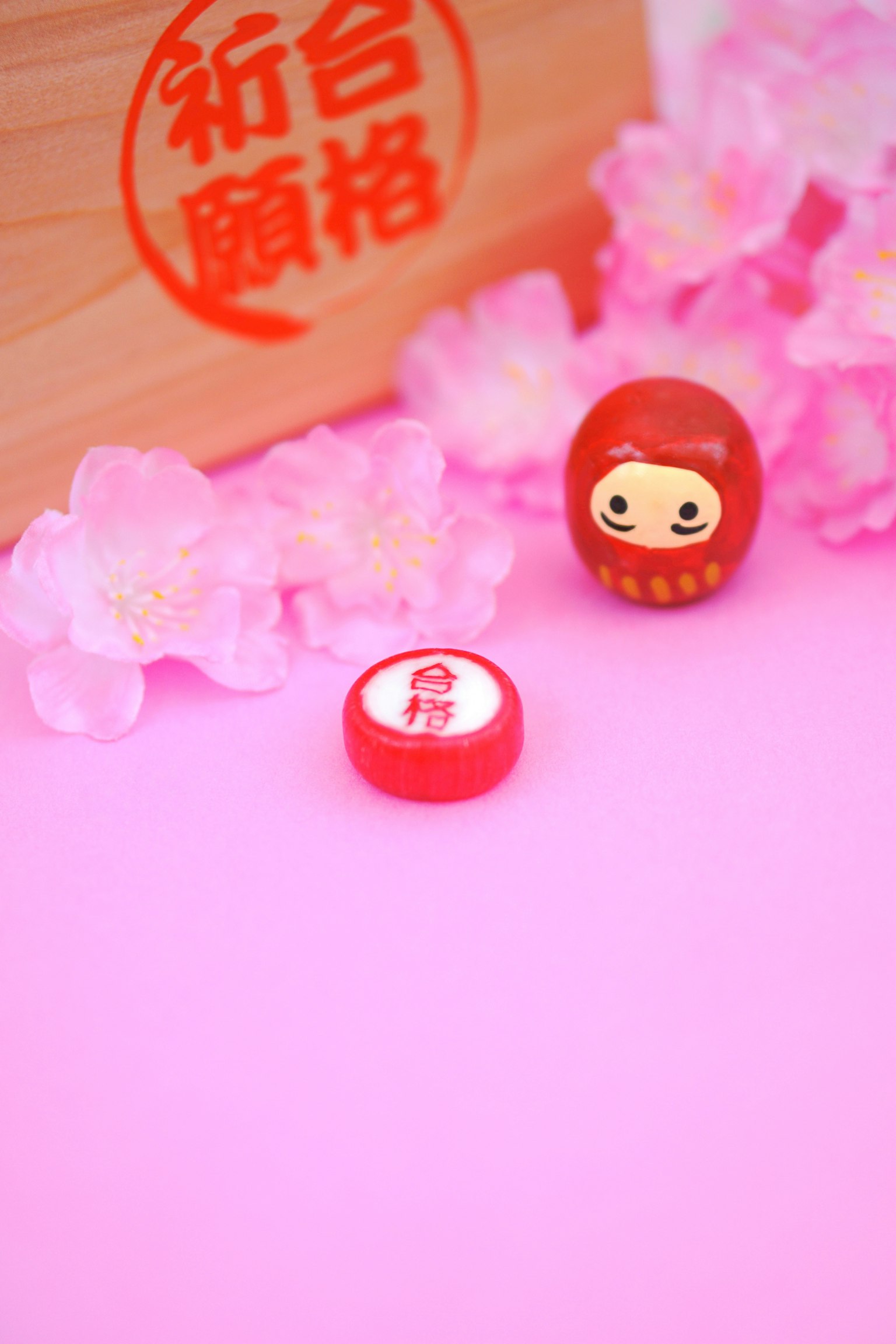 Búp bê daruma đỏ và kẹo đỏ trên nền hồng với hoa anh đào