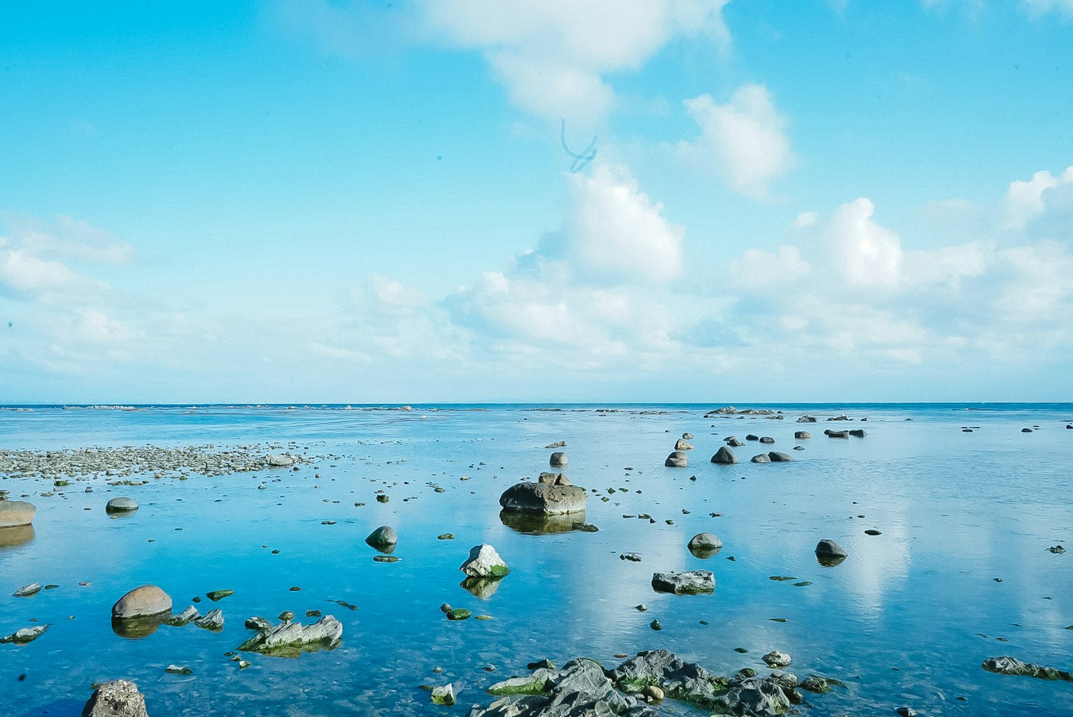 Pemandangan laut dan langit biru dengan batu-batu berserakan di air tenang