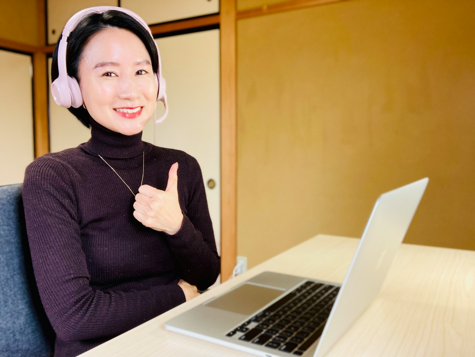 Una donna con cuffie rosa che fa un pollice in su davanti a un laptop