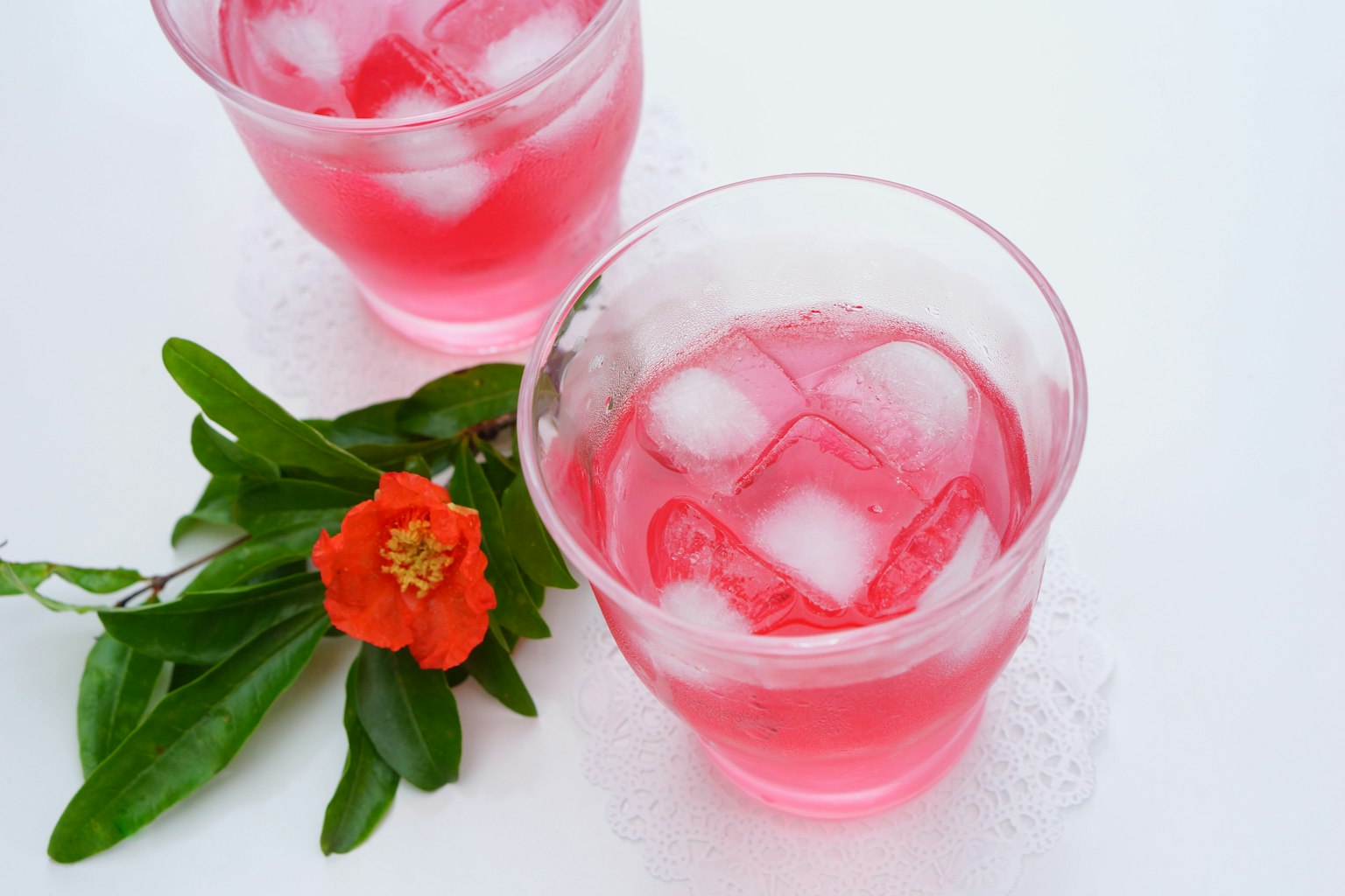 Deux verres de boisson rose avec de la glace accompagnés de feuilles vertes et d'une fleur rouge