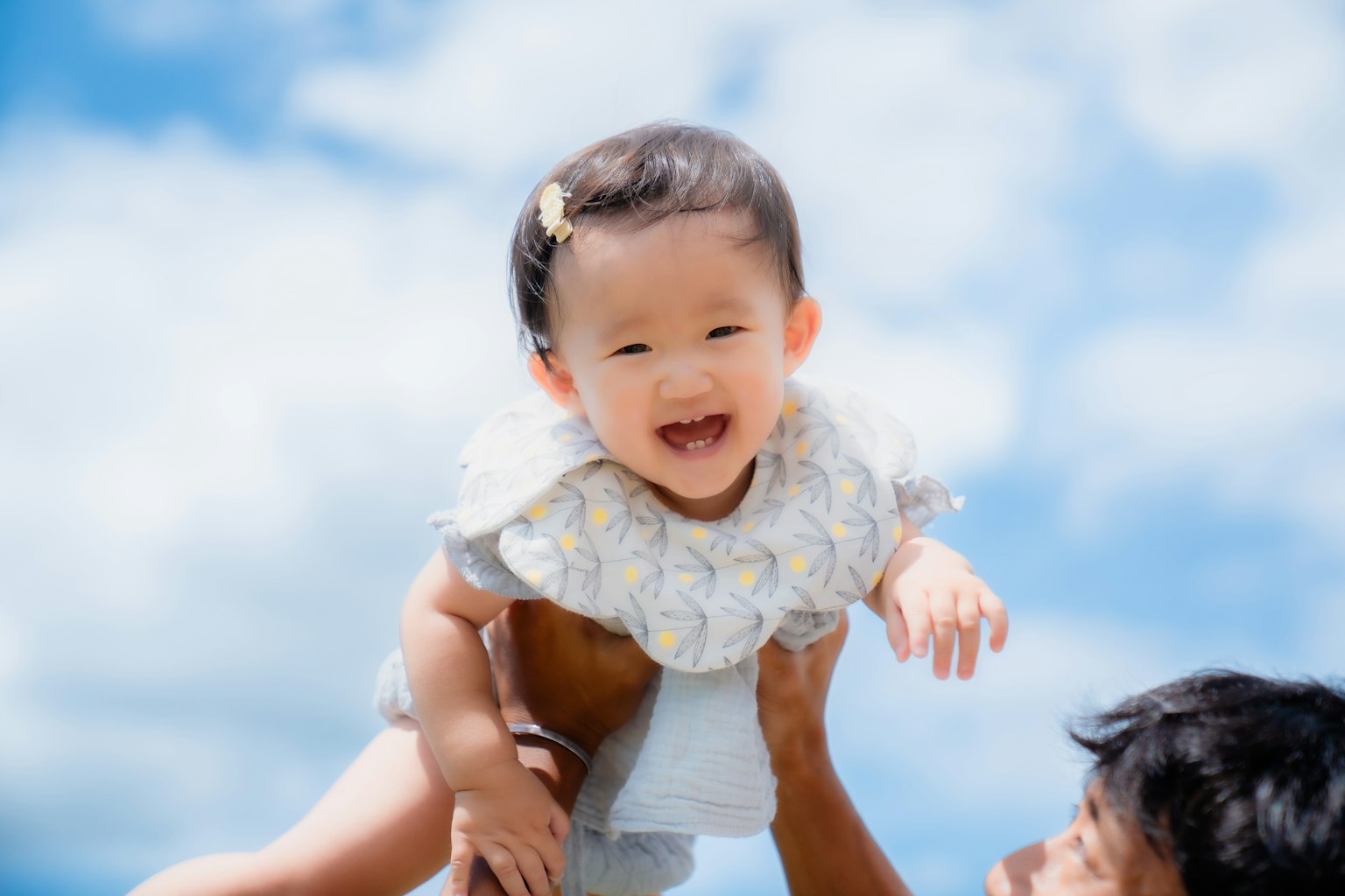 Adulte soulevant un bébé souriant sous un ciel bleu