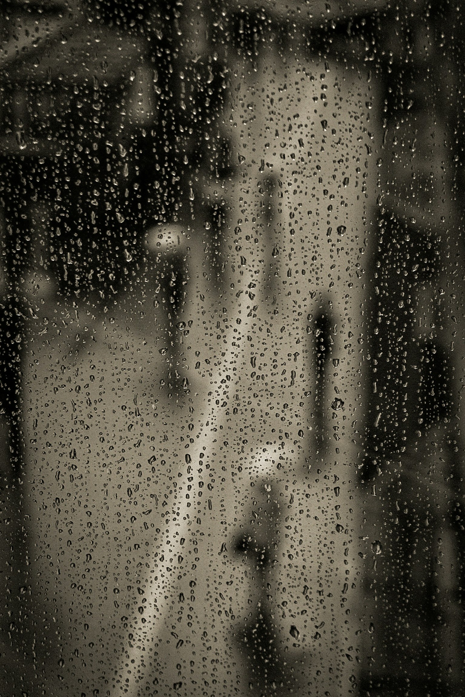 เงาคนที่มองผ่านหน้าต่างที่เปียกน้ำฝนพร้อมกับทิวทัศน์เมืองที่เบลอ