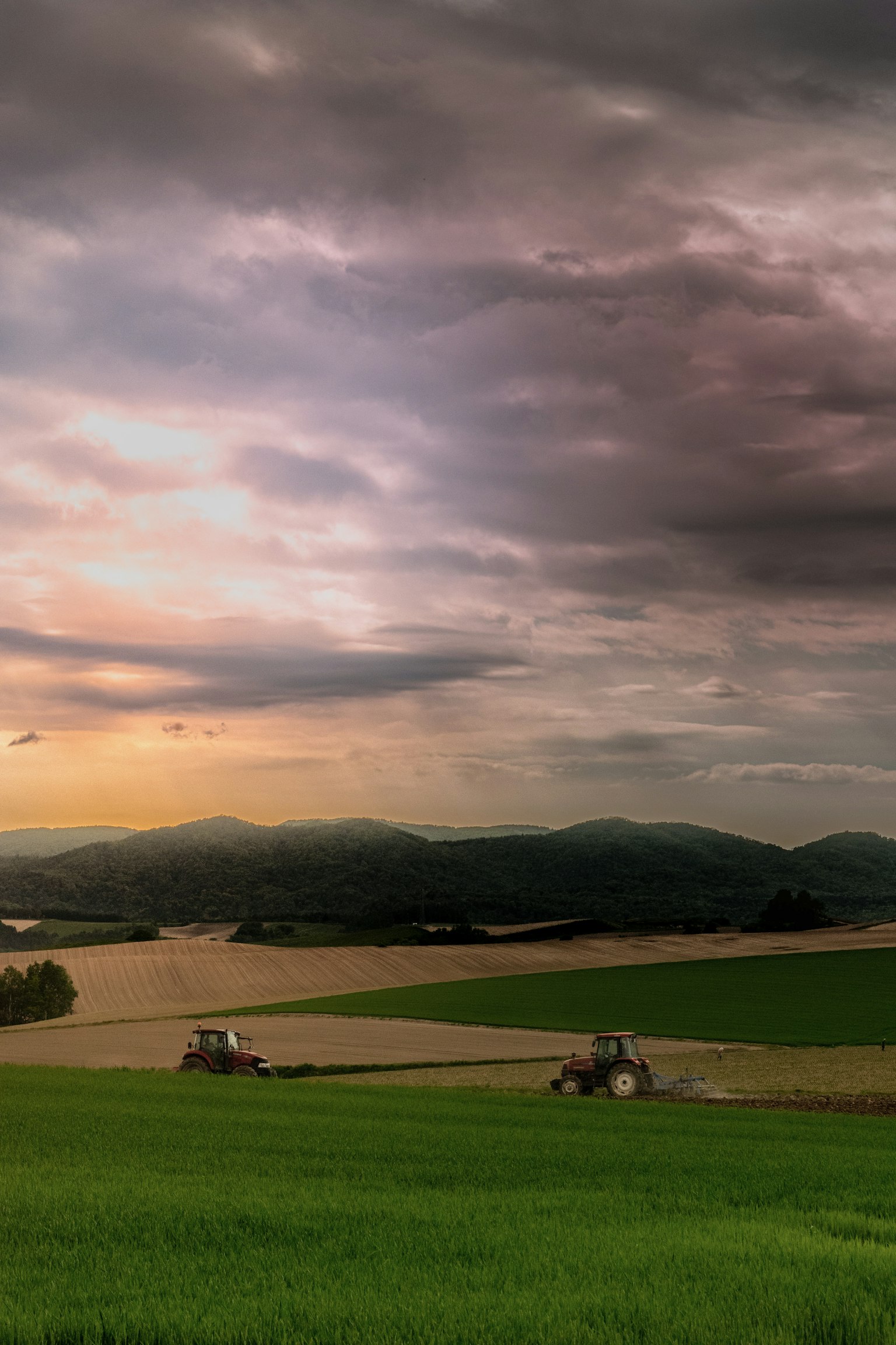 Una vista escénica de campos verdes con tractores bajo un cielo de atardecer