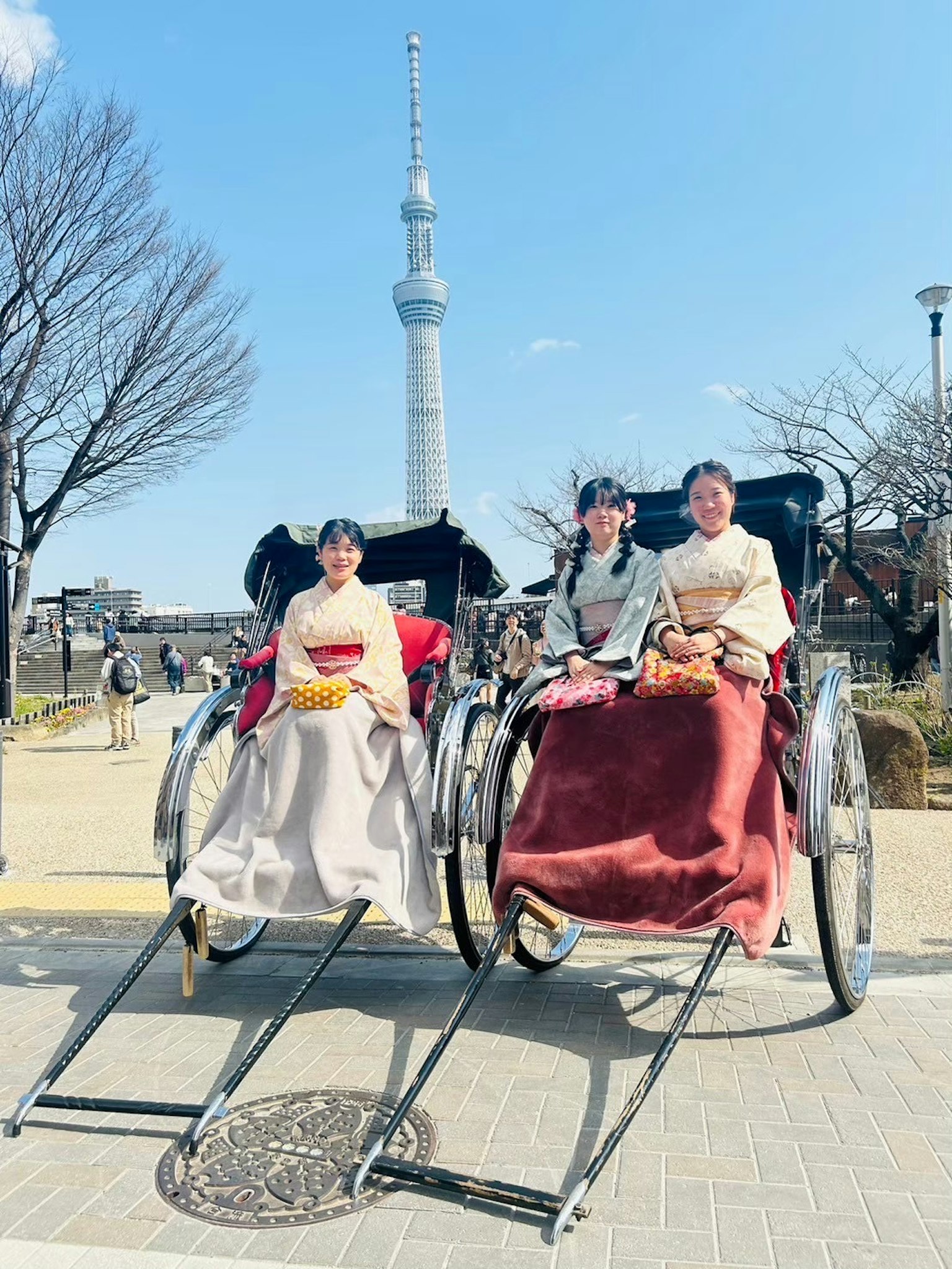 Dos mujeres con ropa tradicional sentadas en rickshaws con la Tokyo Skytree de fondo