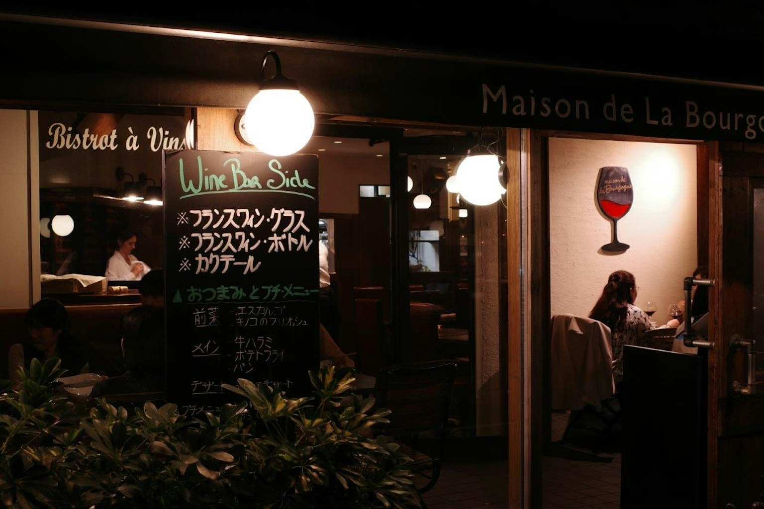 Eksterior restoran Maison de La Bourgogne di malam hari dengan papan menu dan pencahayaan hangat