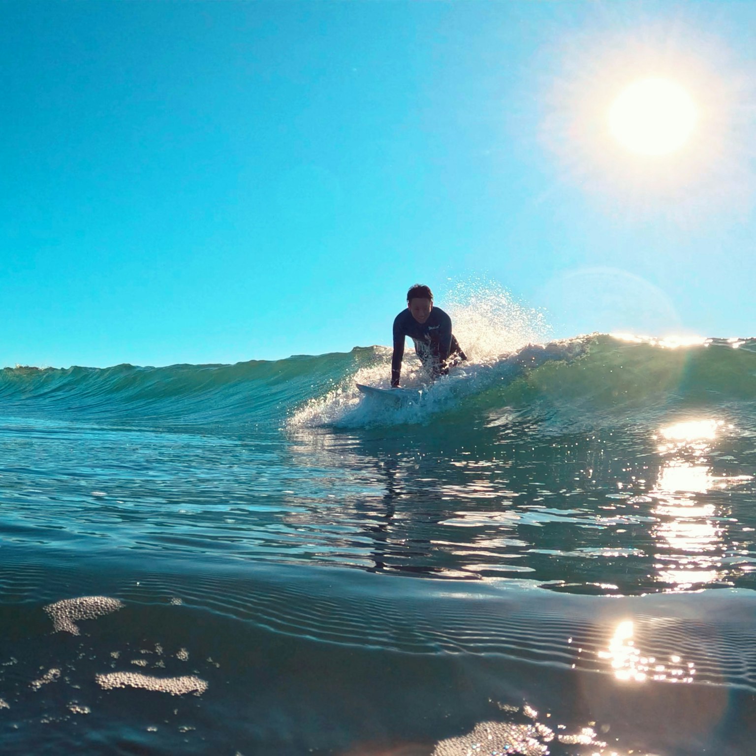 Person surfing on a wave under a bright blue sky